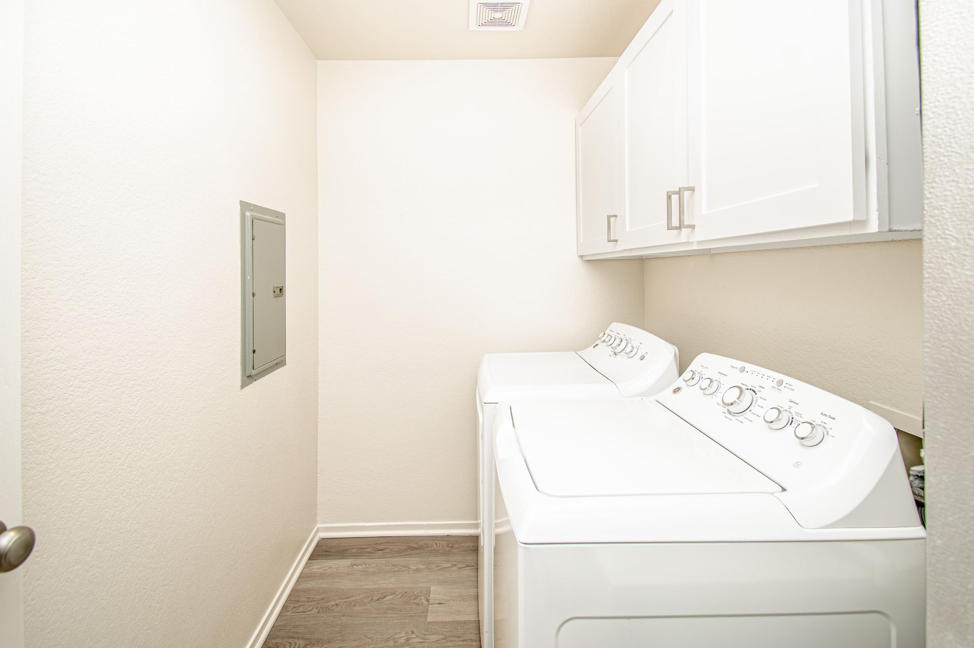 Narrow laundry room with a washer, dryer, and white storage cabinets.