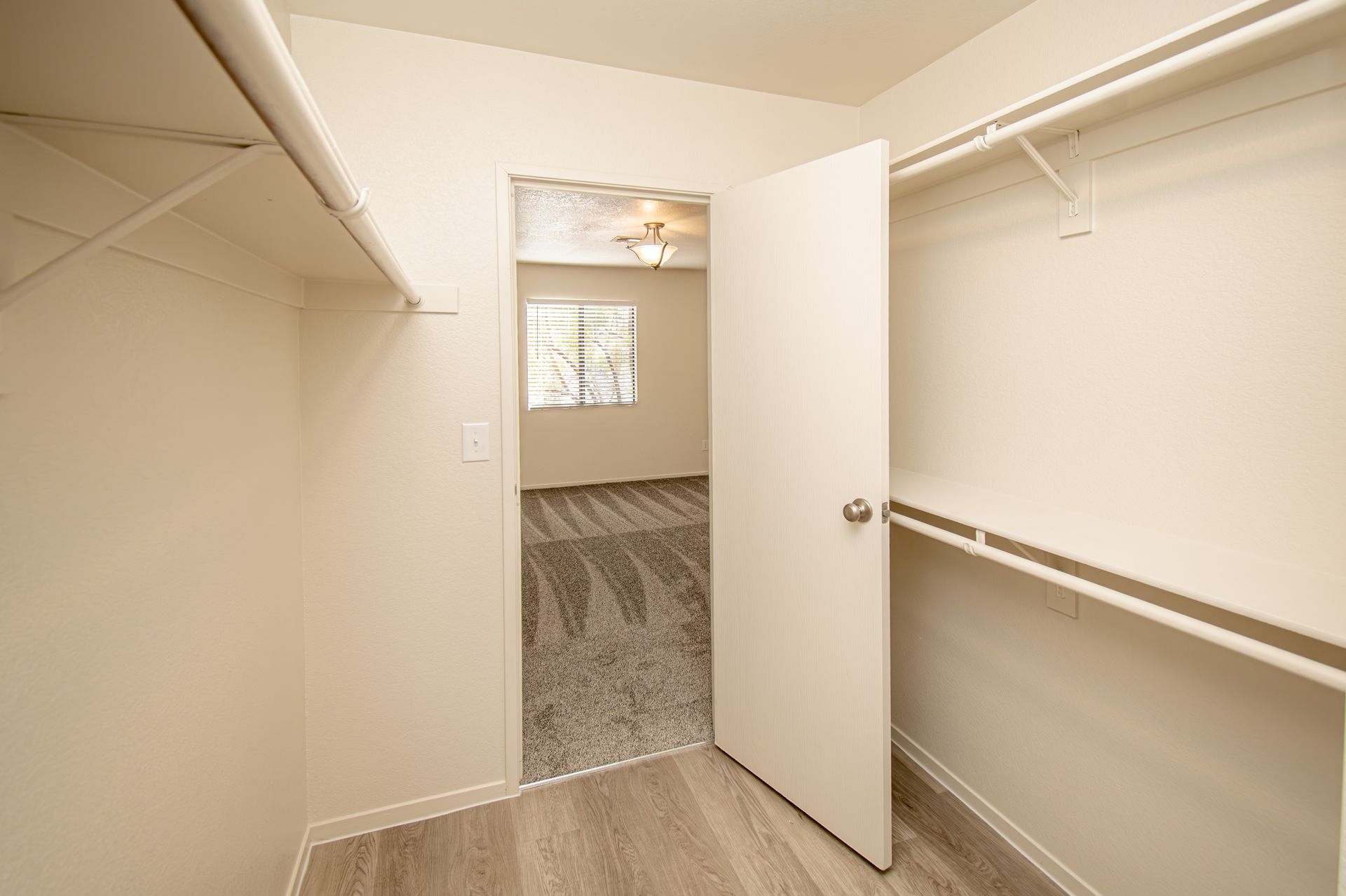 Empty walk-in closet with white shelves and an open door to a carpeted bedroom.