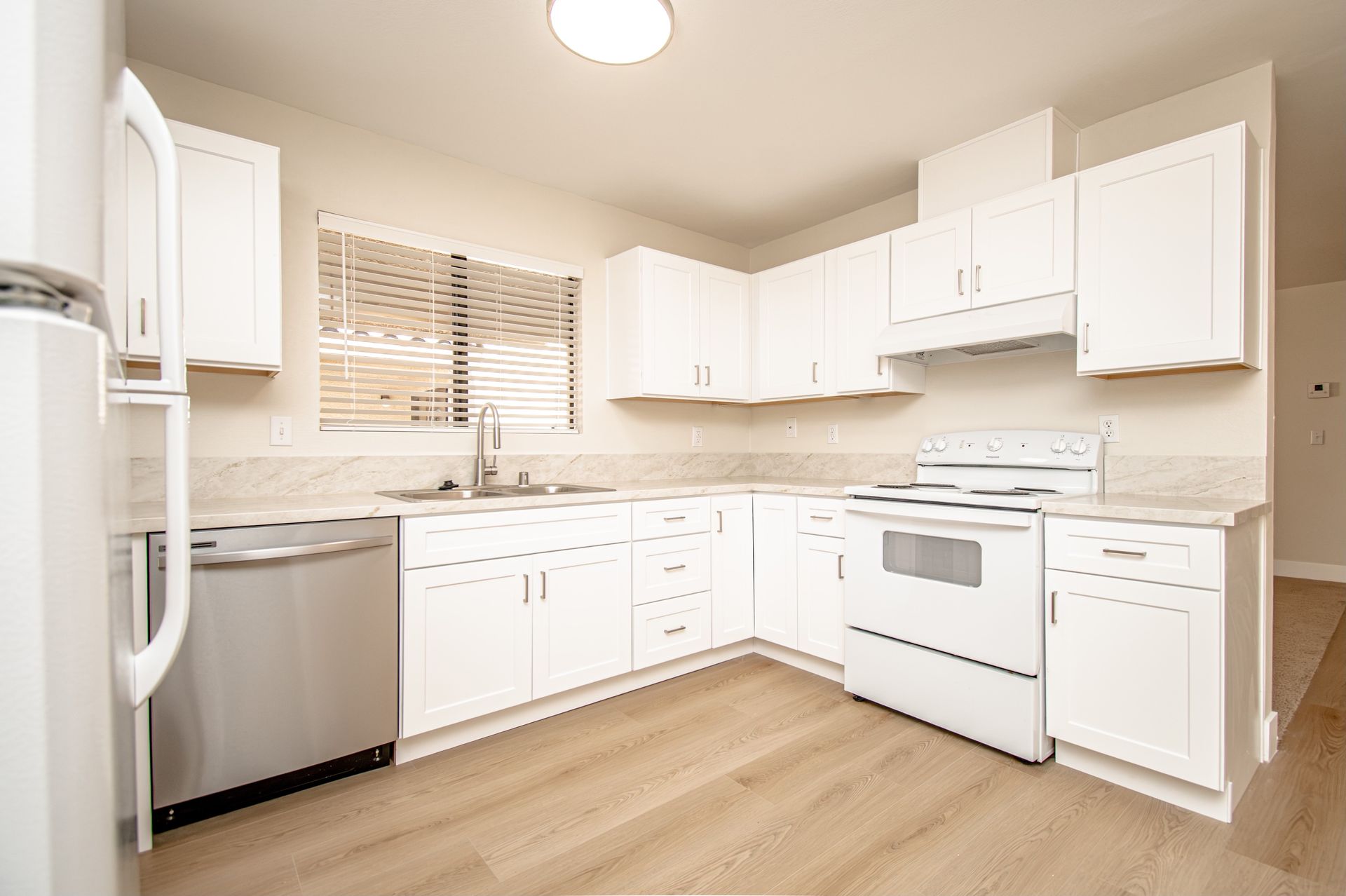 Bright white kitchen with stainless steel dishwasher, white cabinets, and wood flooring