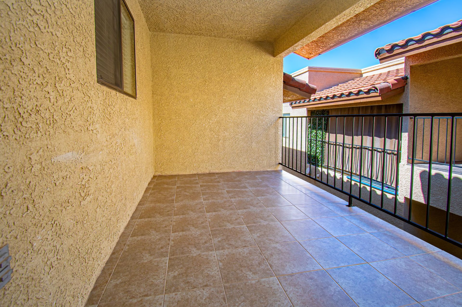Covered balcony with beige tile floor and black railing overlooking neighboring buildings.