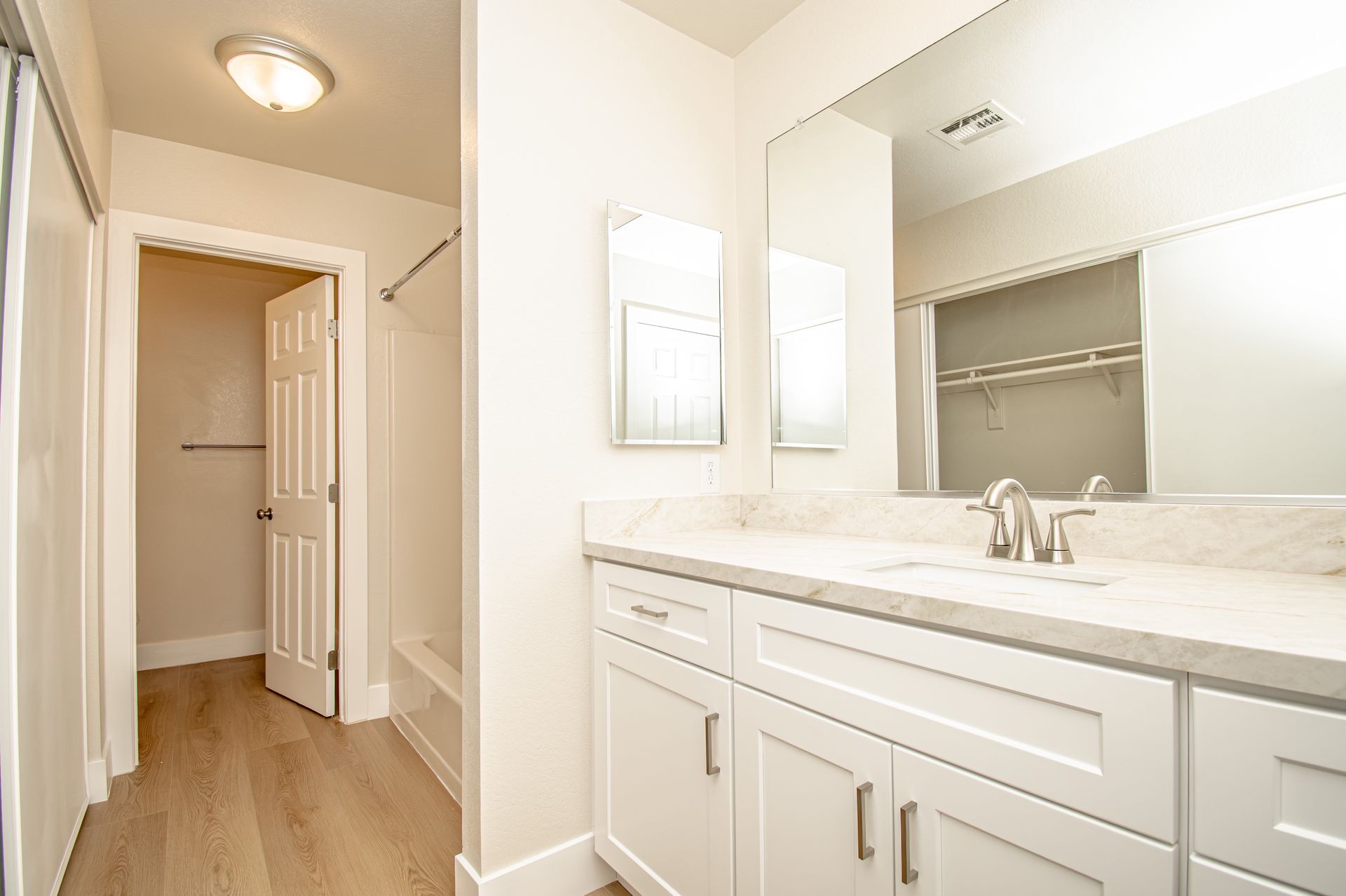 Bright bathroom vanity with mirror, white cabinets, and hallway view in the background