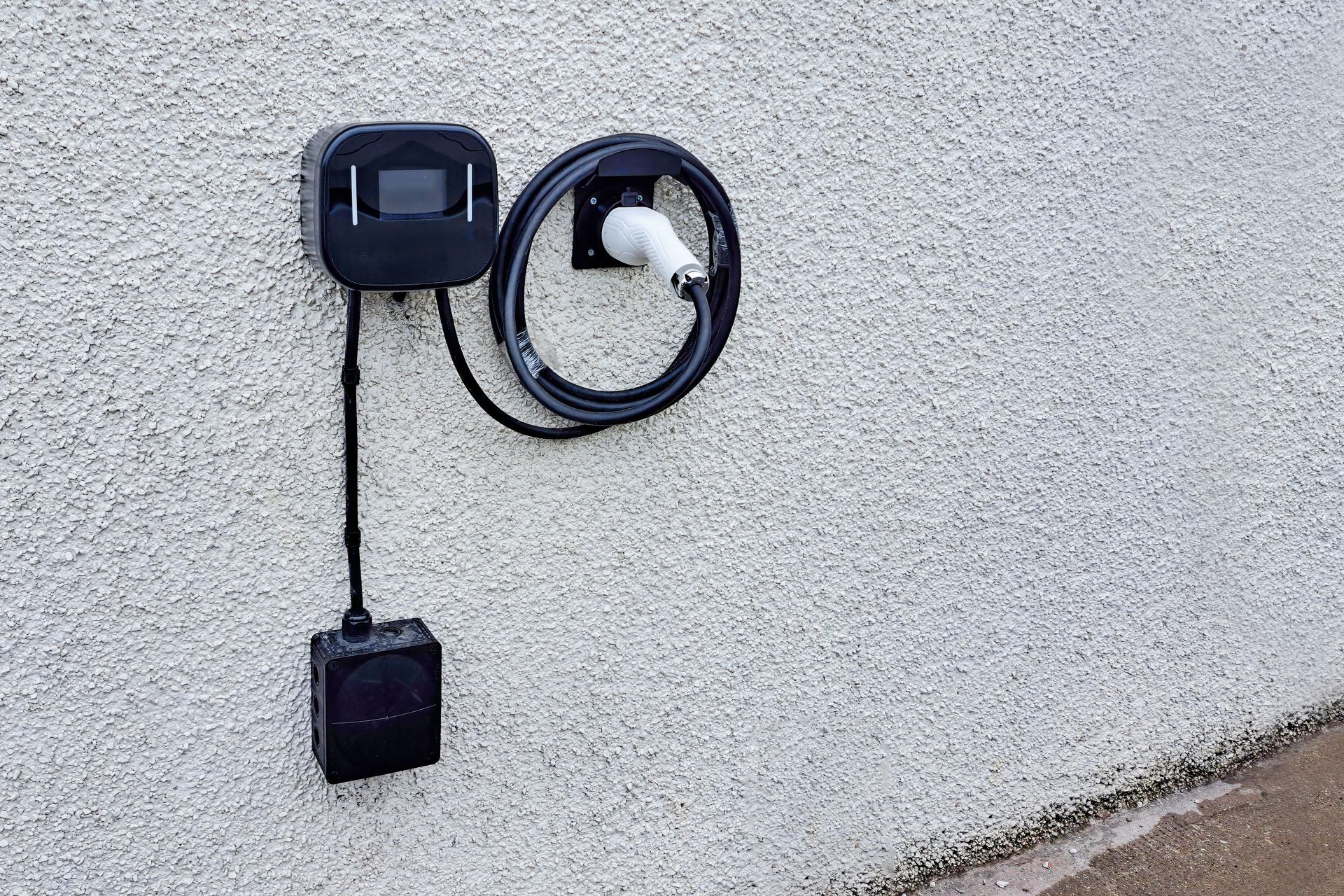 Outdoor wall-mounted EV charging station with black cable coiled on a white stucco wall.