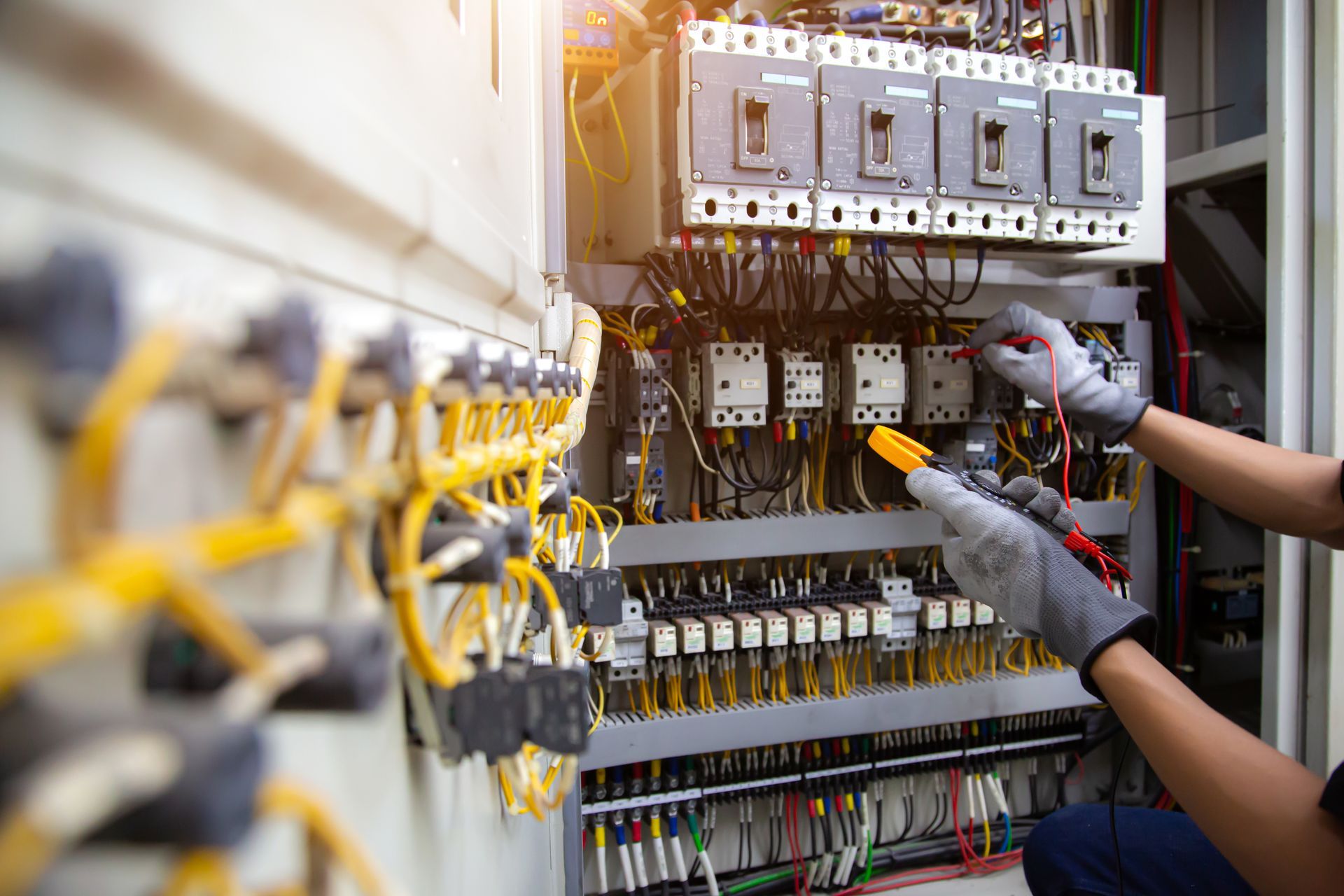 Technician wiring an electrical control panel with tools in a utility cabinet.