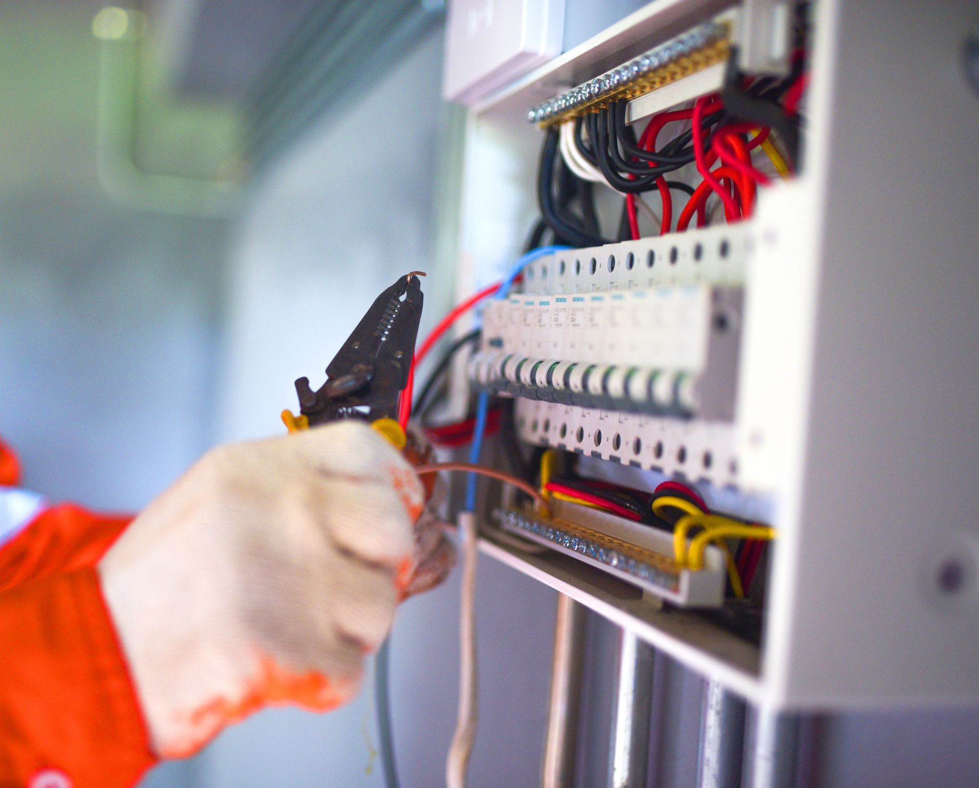 Technician using pliers to work on exposed wiring inside an electrical control panel.
