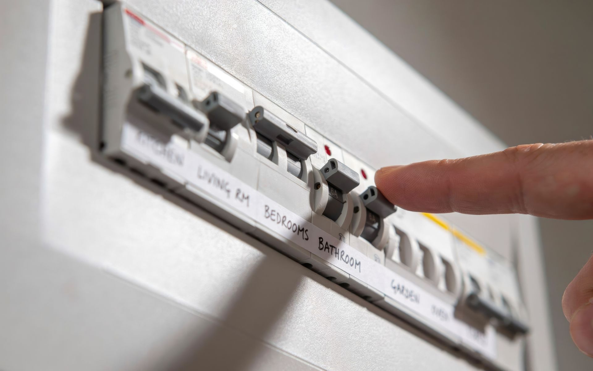 Finger pressing a row of wall-mounted circuit breakers on a white electrical panel.
