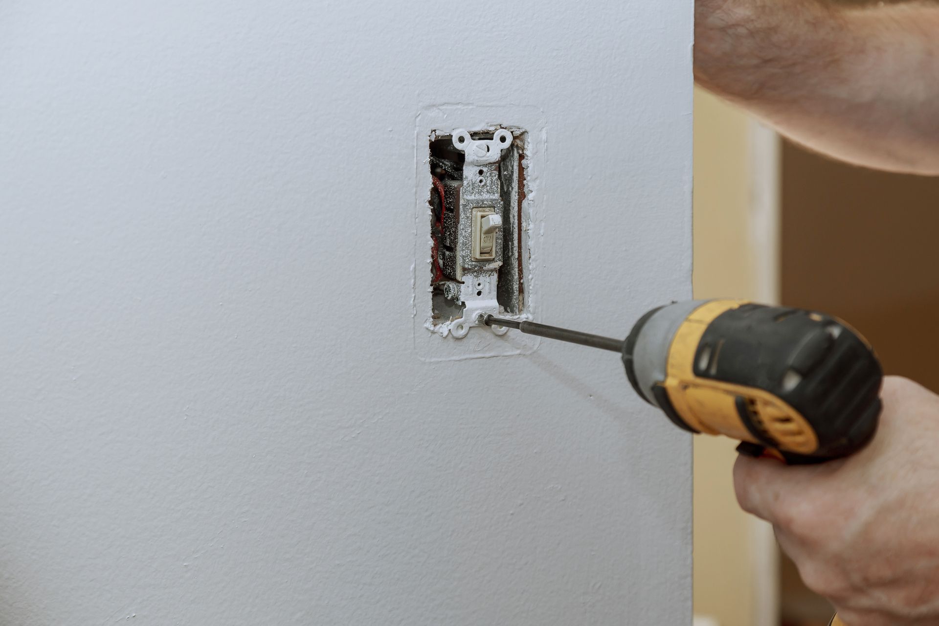 Hand drilling a wall outlet box with a screwdriver, close-up of electrical repair work.
