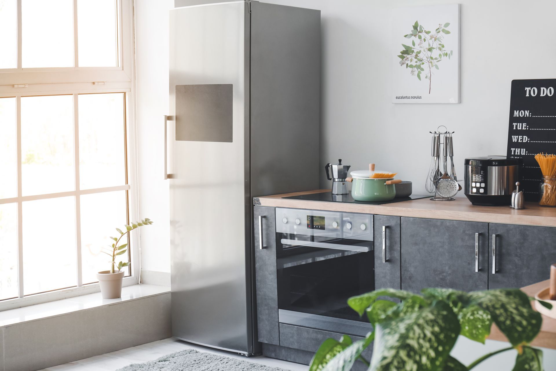 Bright modern kitchen with stainless steel appliances, gray cabinets, and a sunlit window.