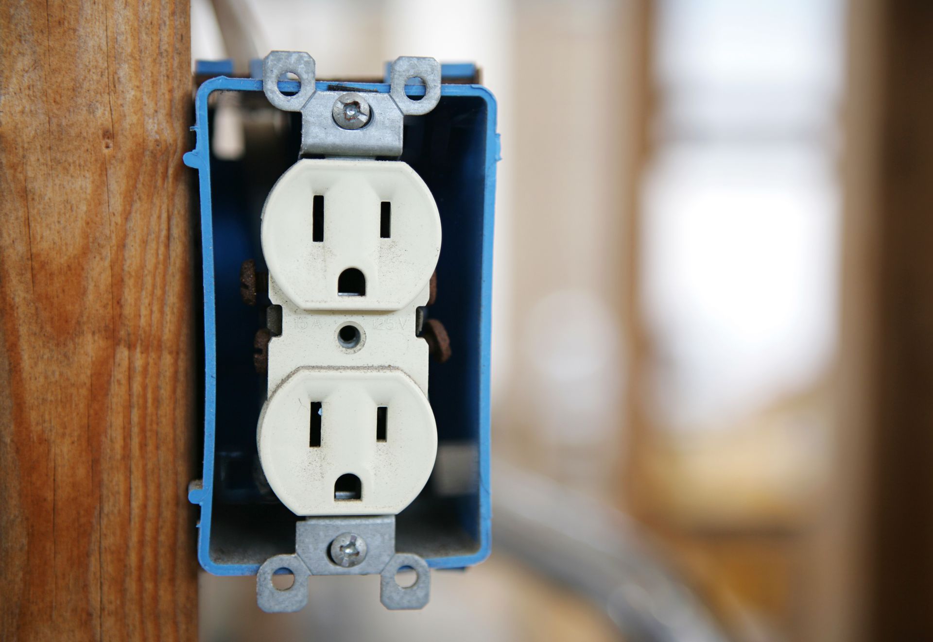 Two white electrical outlets in a blue wall box on a wooden post, outdoors.