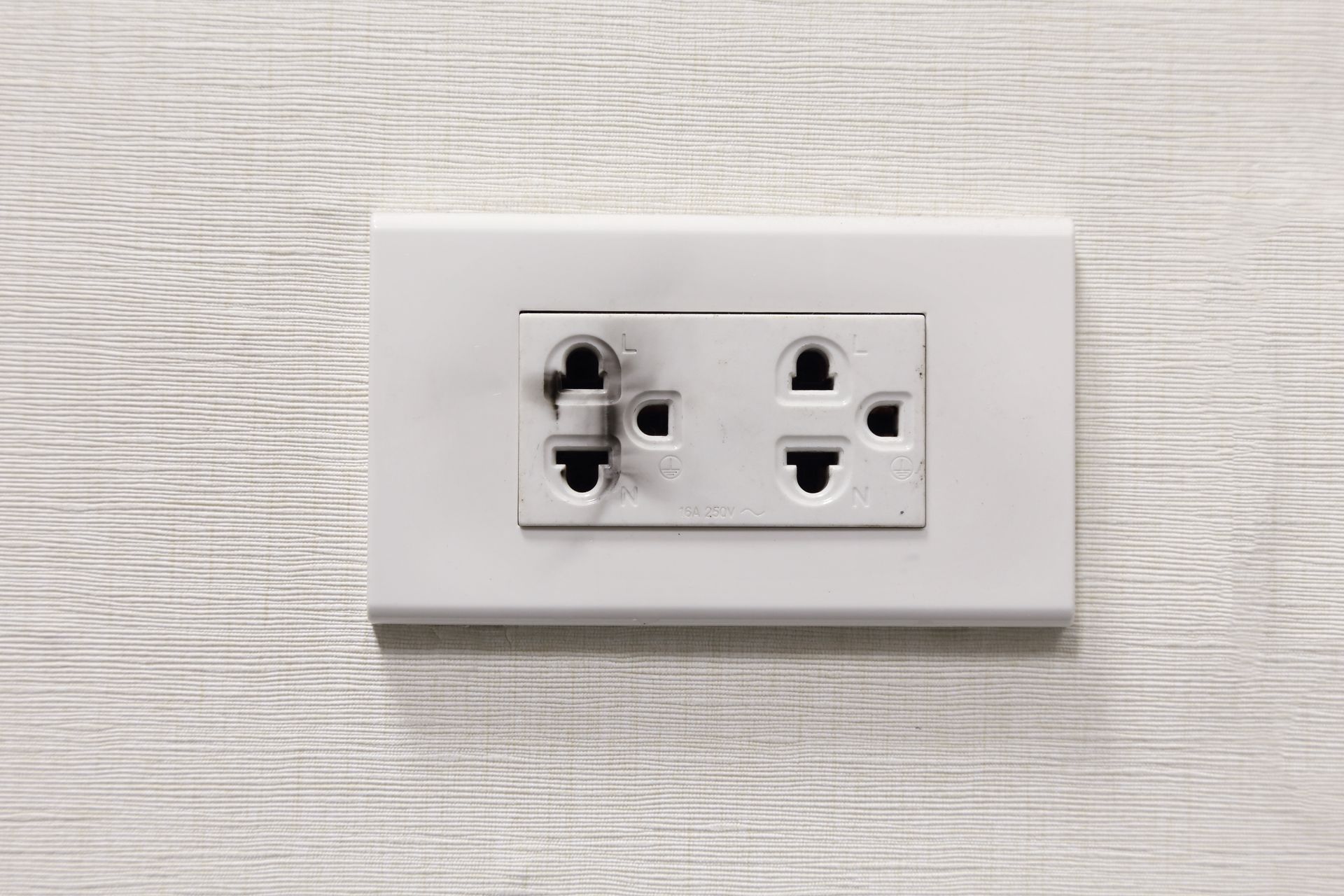 White electrical outlet on a light textured wall, with one socket damaged and darkened.