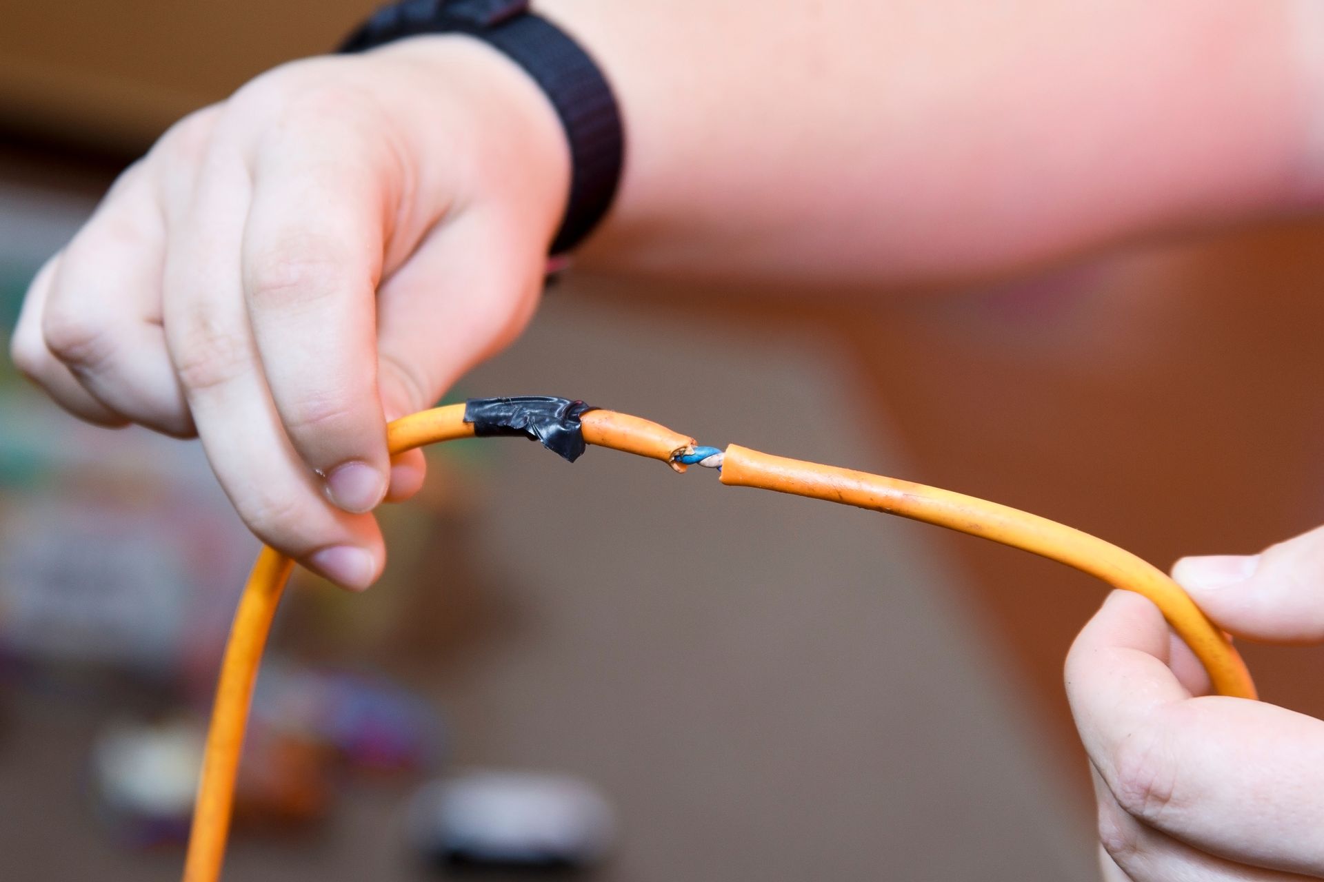 Hands holding a damaged orange cable with exposed wiring.