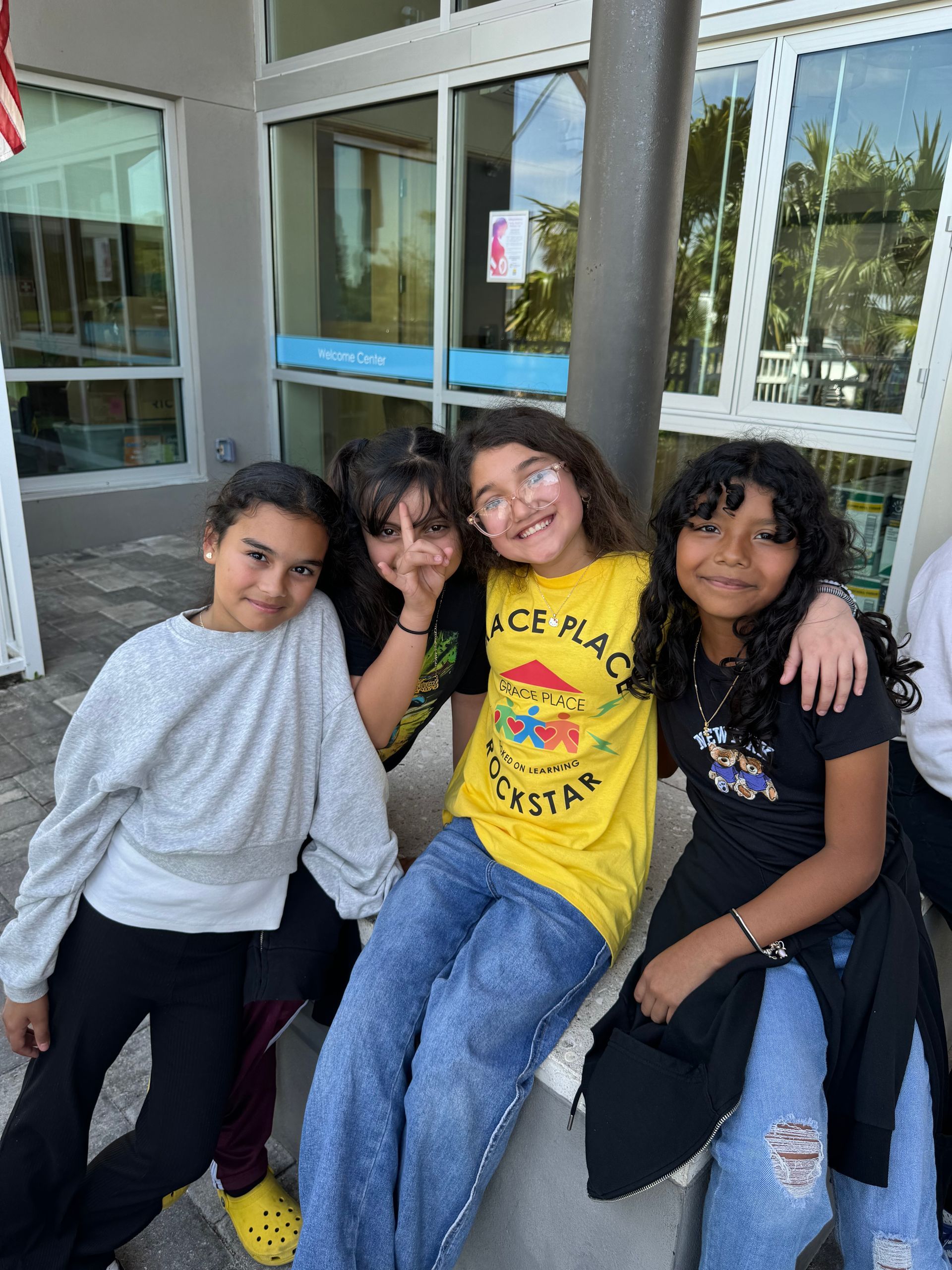 Four young girls smiling and posing together outside a building.