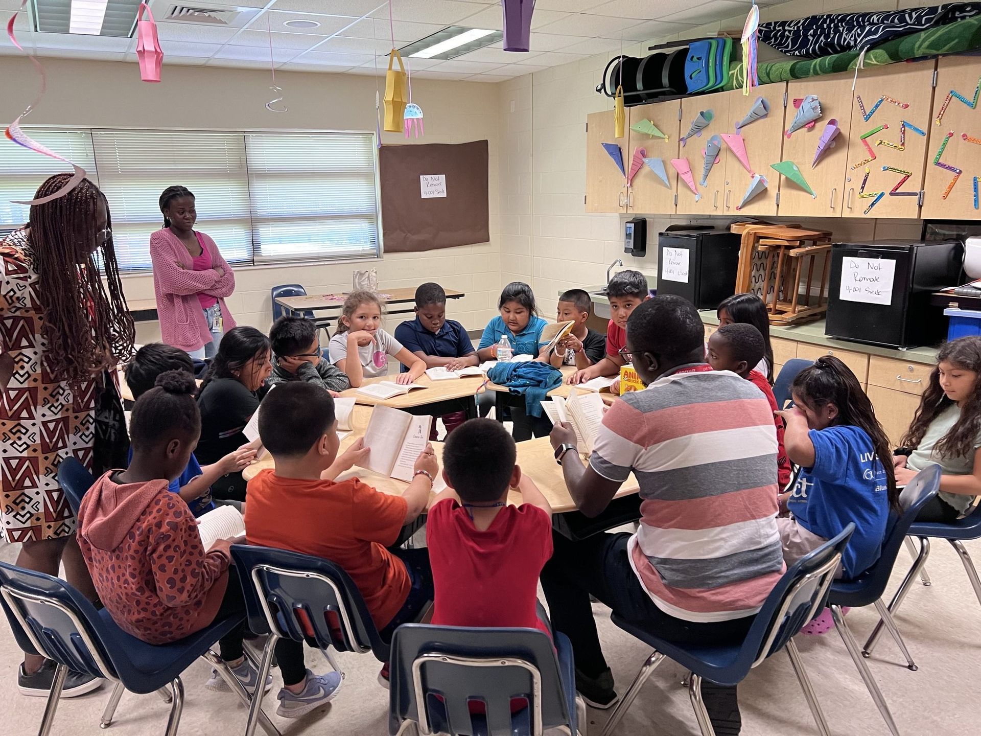 A group of children and two adults in a classroom reading and discussing.