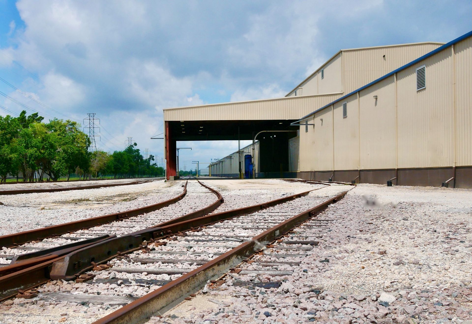 Train tracks leading to a large industrial building under a cloudy sky.