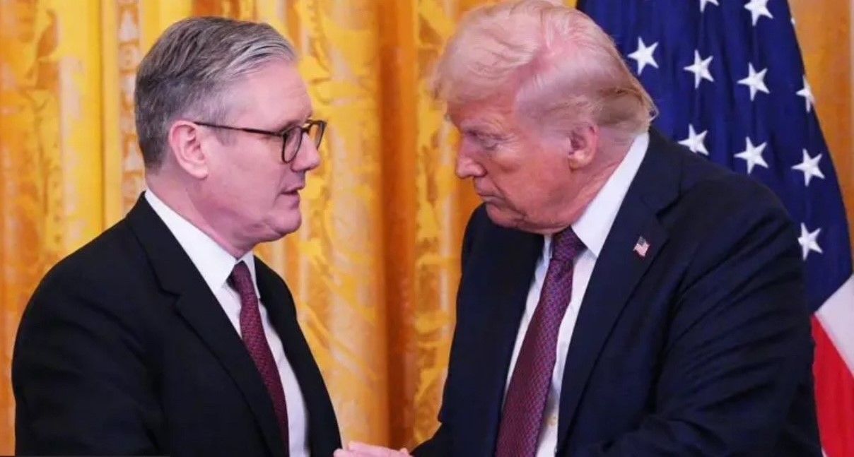 Two men in suits: Donald Trump and a man with glasses, talking in front of a US flag.