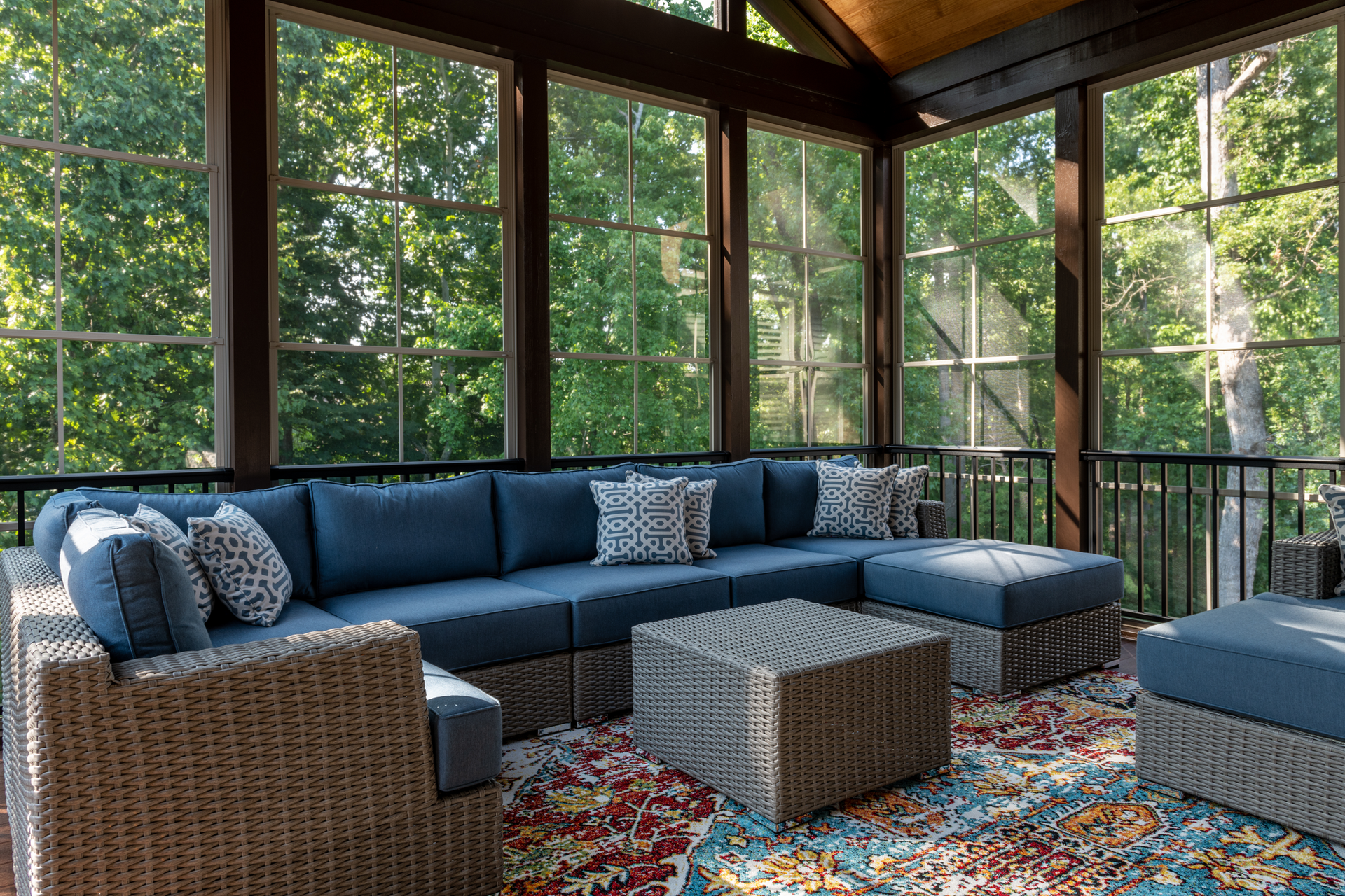 A screened in porch with wicker furniture and a rug.