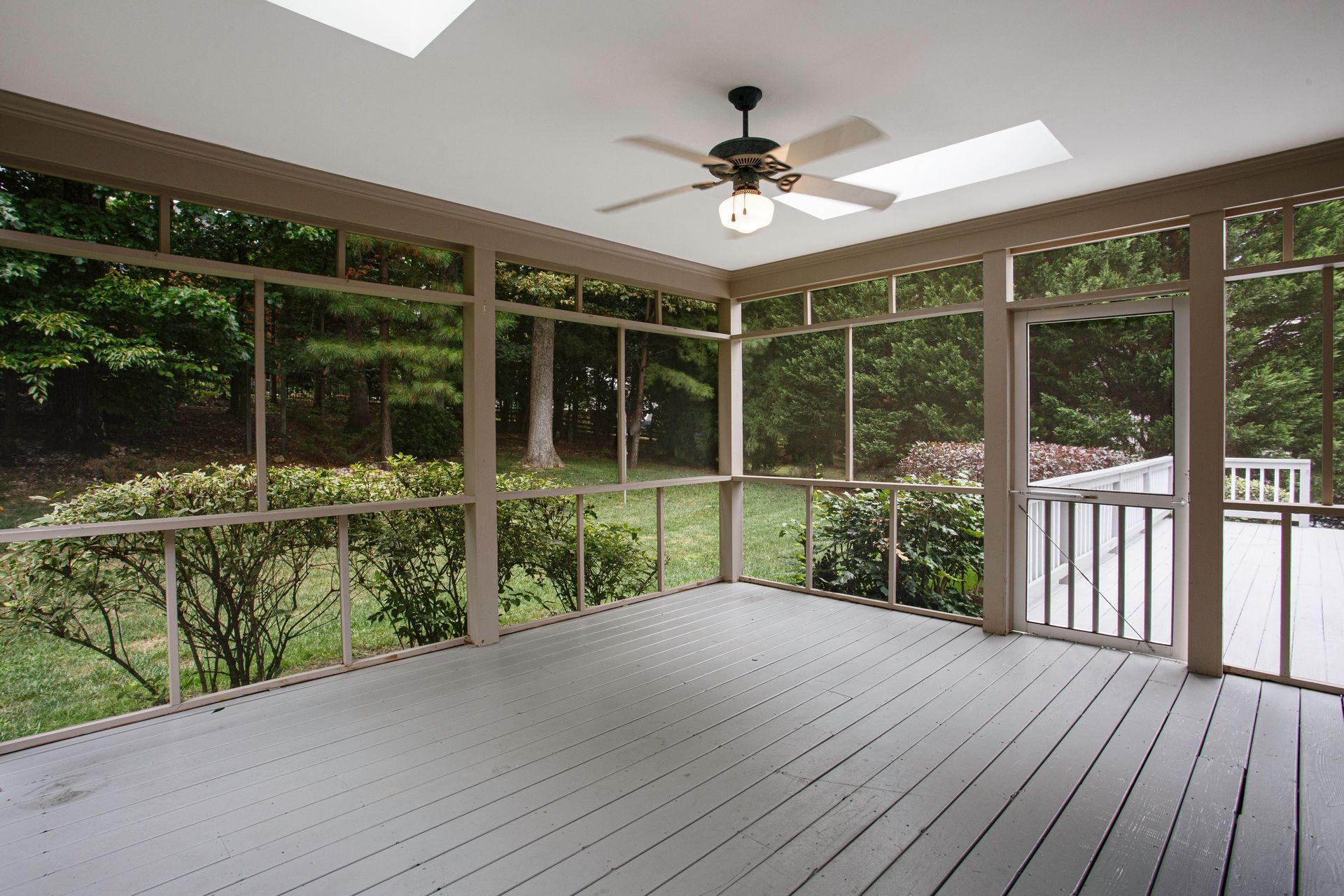 An empty screened in porch with a ceiling fan