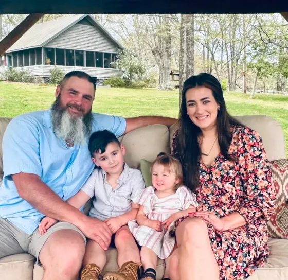A family is posing for a picture while sitting on a couch in front of a house.