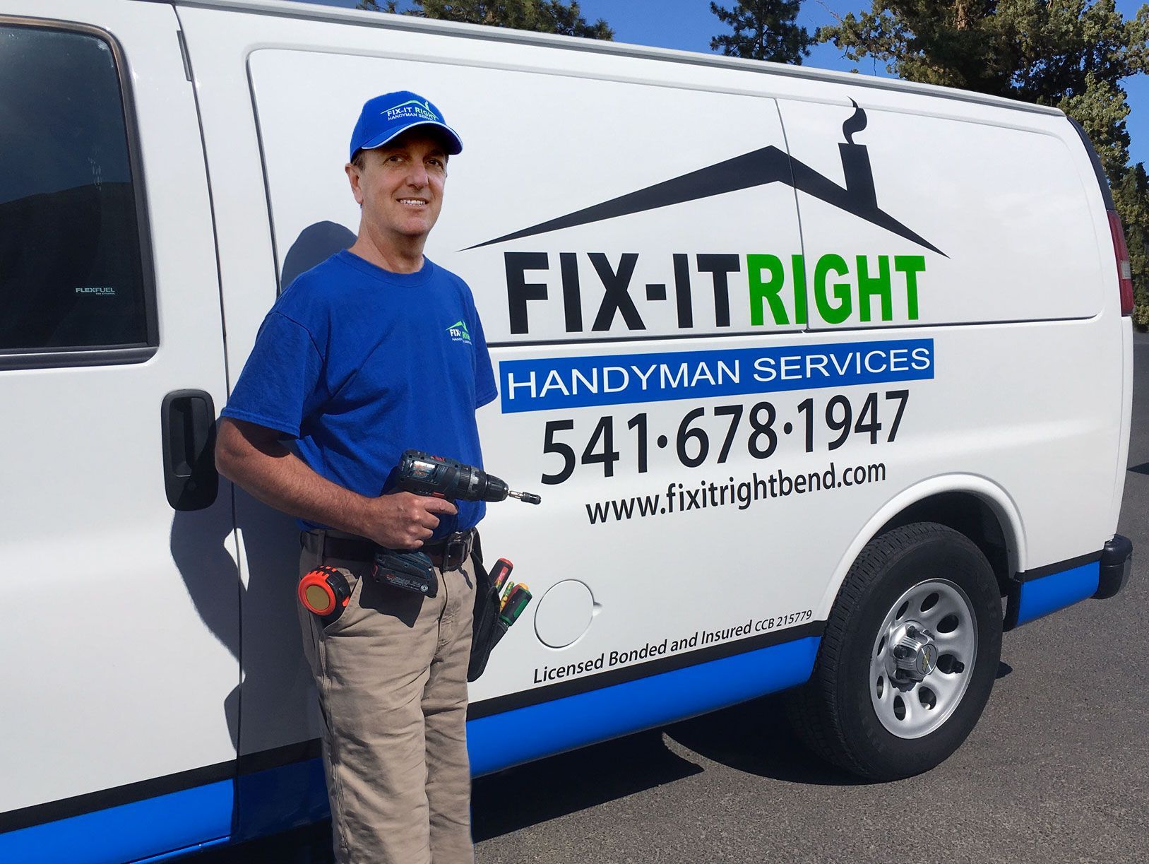 A person wearing a blue shirt and cap holding a power drill stands in front of a white 