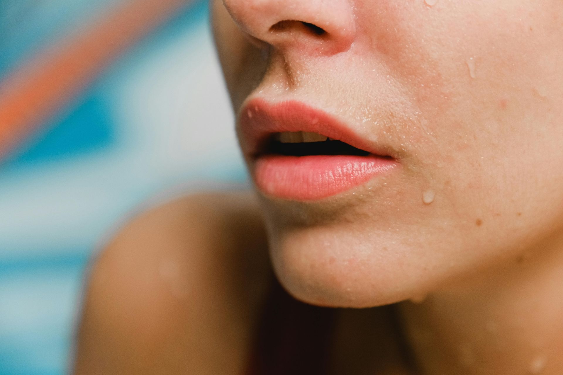 Red-haired woman with wide eyes, holding pink lip balm, against a blue background.