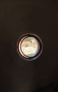 Oblò rotondo in una porta scura, con luce naturale intensa all'esterno.