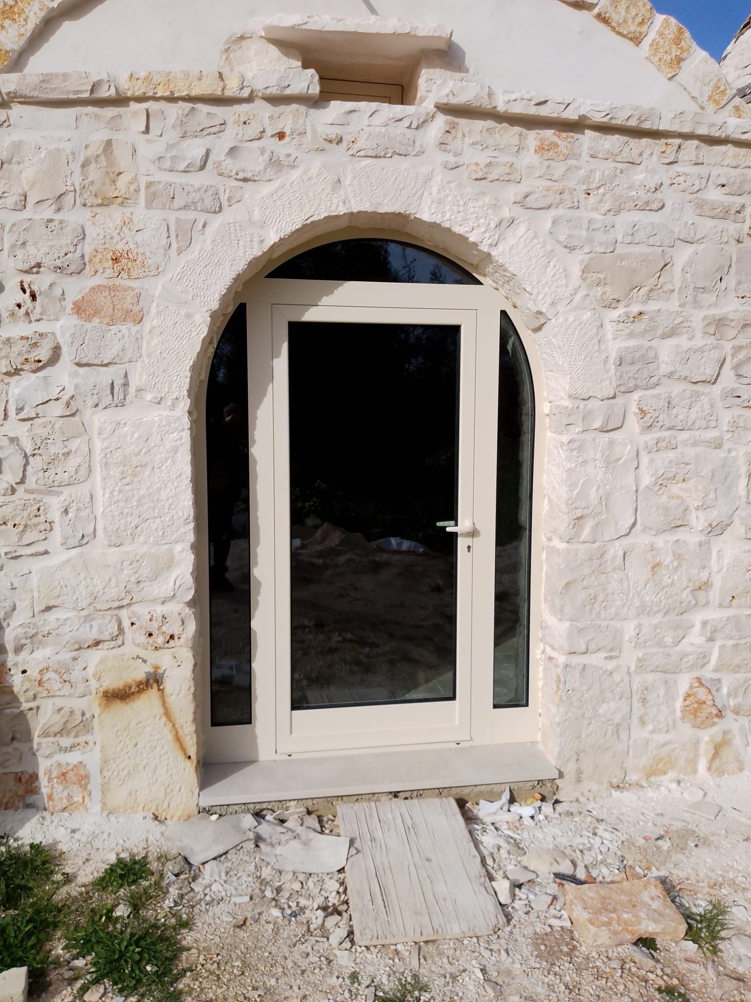 Ingresso di un edificio in pietra con porta bianca ad arco e interno scuro alle sue spalle.