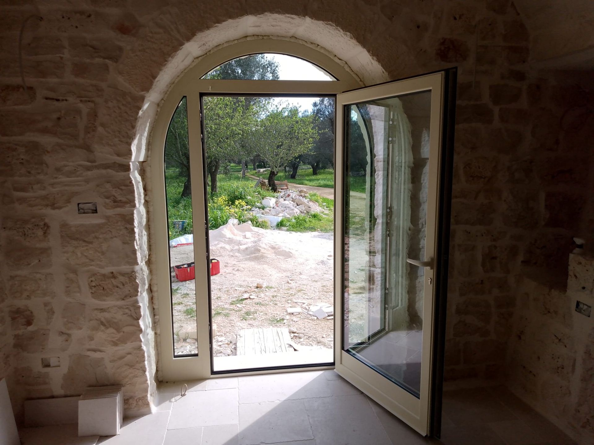 Un portale in pietra aperto con porta a vetri conduce a un sentiero soleggiato in giardino.