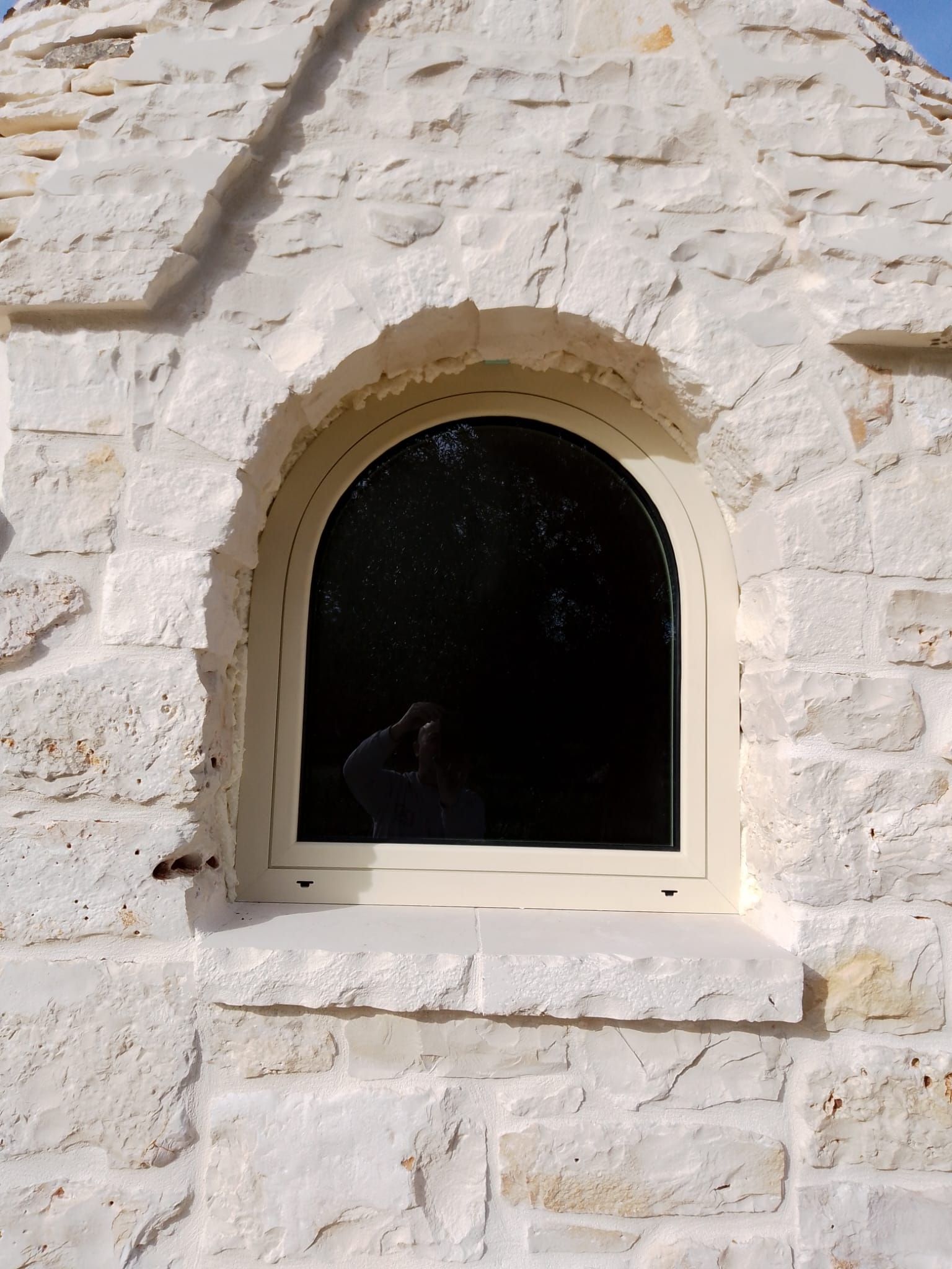 Finestra ad arco in una parete di pietra bianca, con un interno scuro visibile dall'interno.