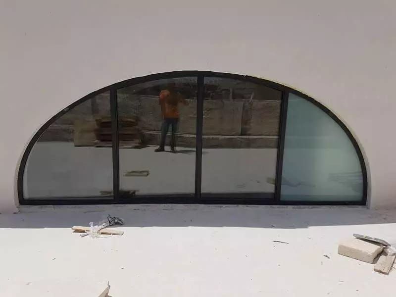 Finestra ad arco con cornice nera riflessa in una parete bianca, con una persona in piedi all'esterno.