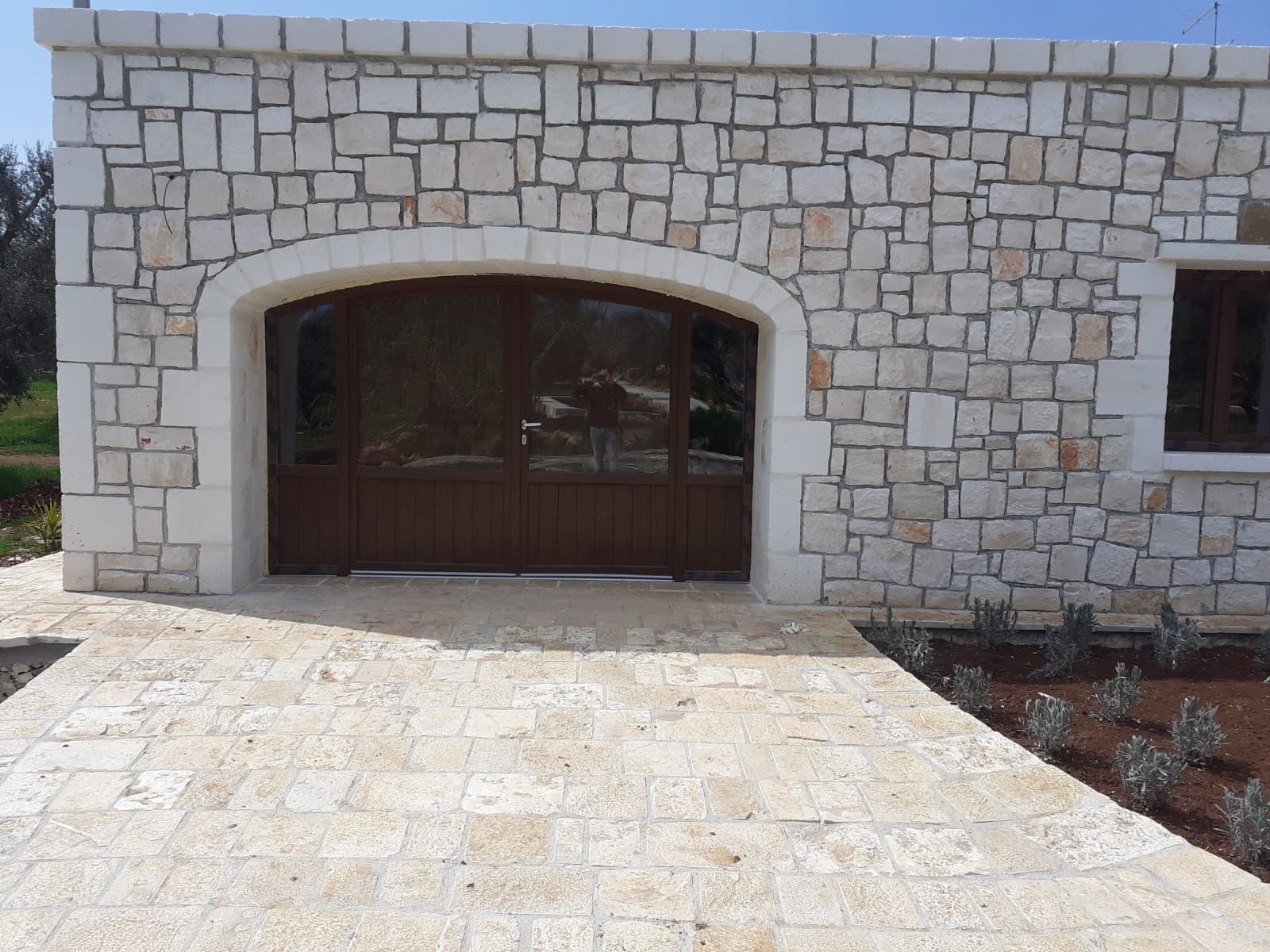 Facciata della casa in pietra con doppie porte ad arco in legno e vialetto pavimentato.