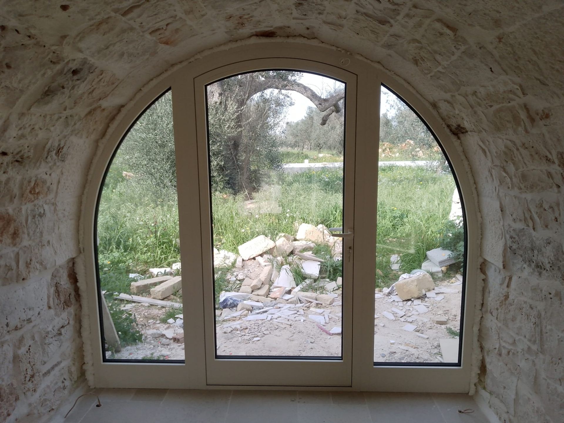 Finestra ad arco in pietra che si affaccia su un prato e sulle rocce sullo sfondo.