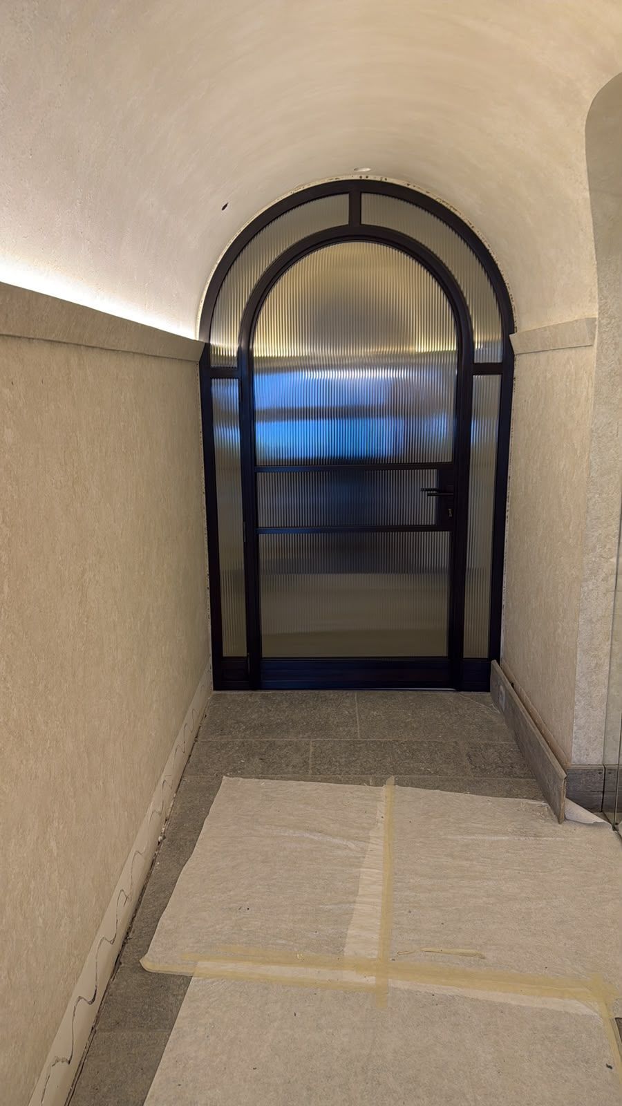 Porta ad arco in fondo a uno stretto corridoio, con una finestra o una porta illuminata di blu al di là.