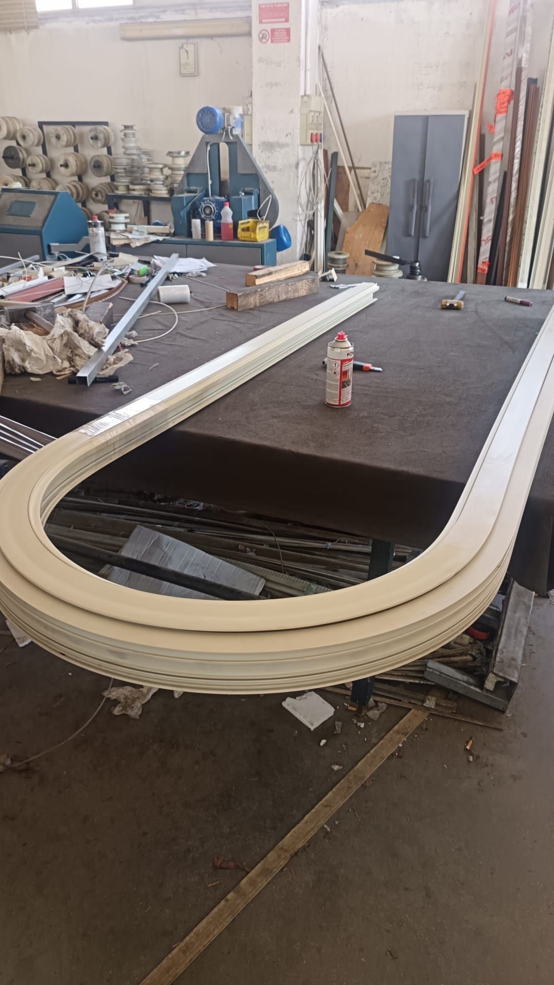 In un'officina, un grande tavolo di legno curvo è circondato da attrezzi e materiali.