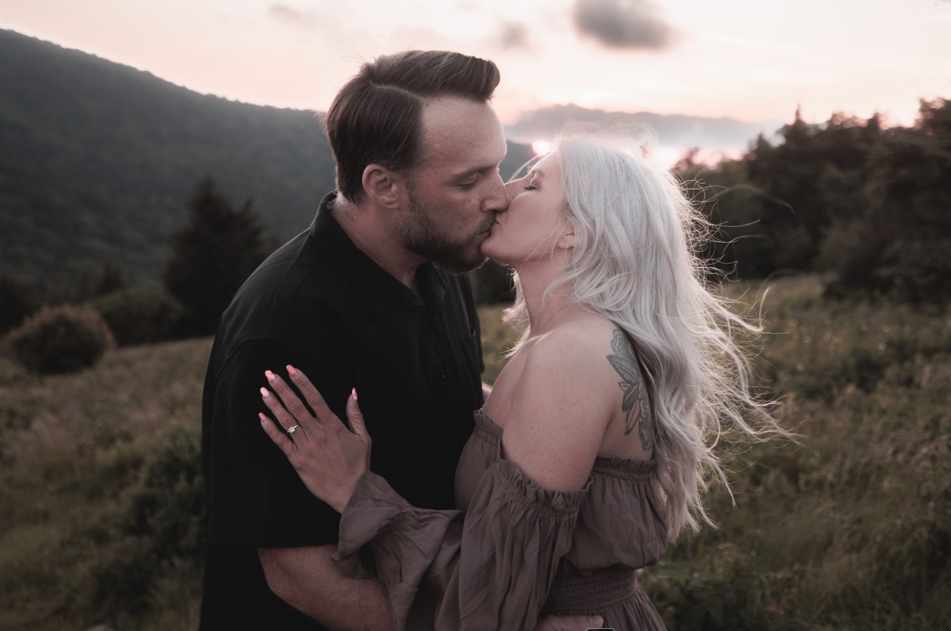 Brandon and Grace sharing a kiss at sunset in the mountains