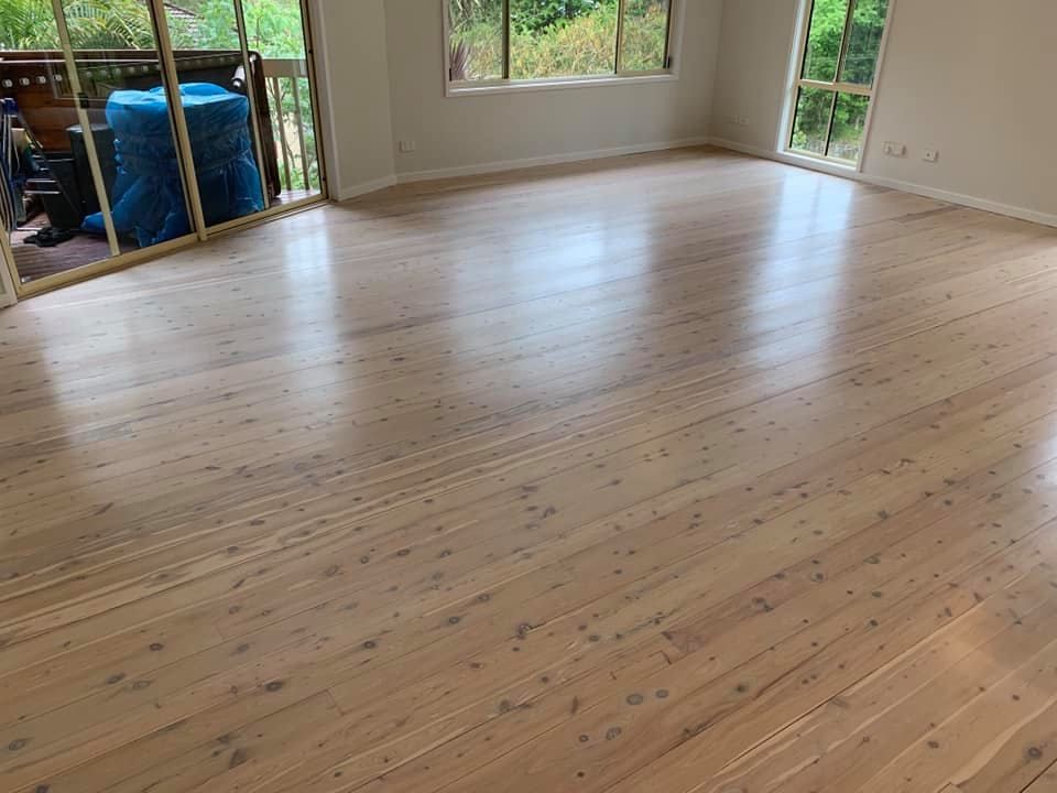 A bright room featuring light-toned, natural wood flooring, white walls, and large windows looking out onto greenery — Custom Floor Sanding In Somersby, NSW