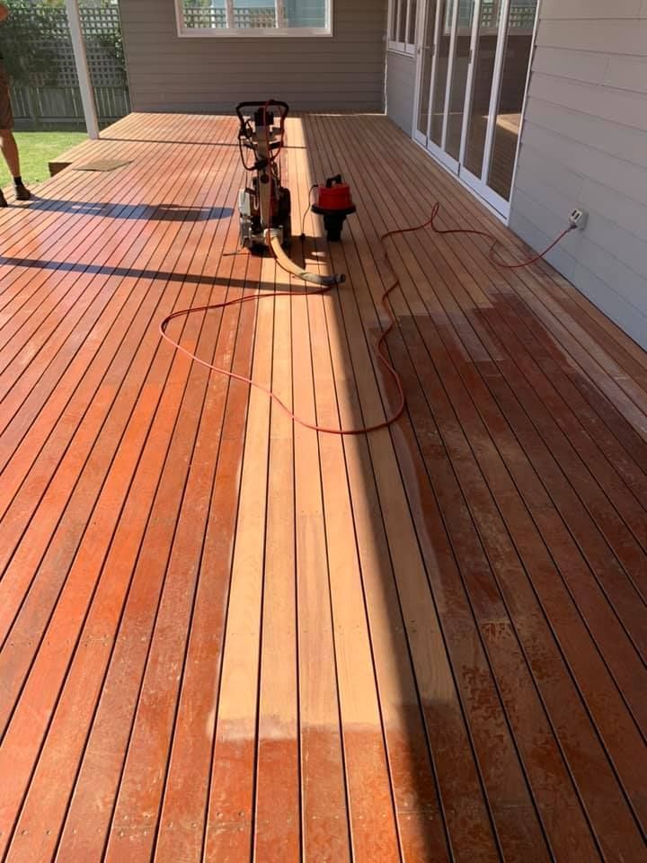 A wooden deck being refinished with a sanding machine, showing a lighter, sanded strip in contrast to the dark deck — Custom Floor Sanding In Somersby, NSW
