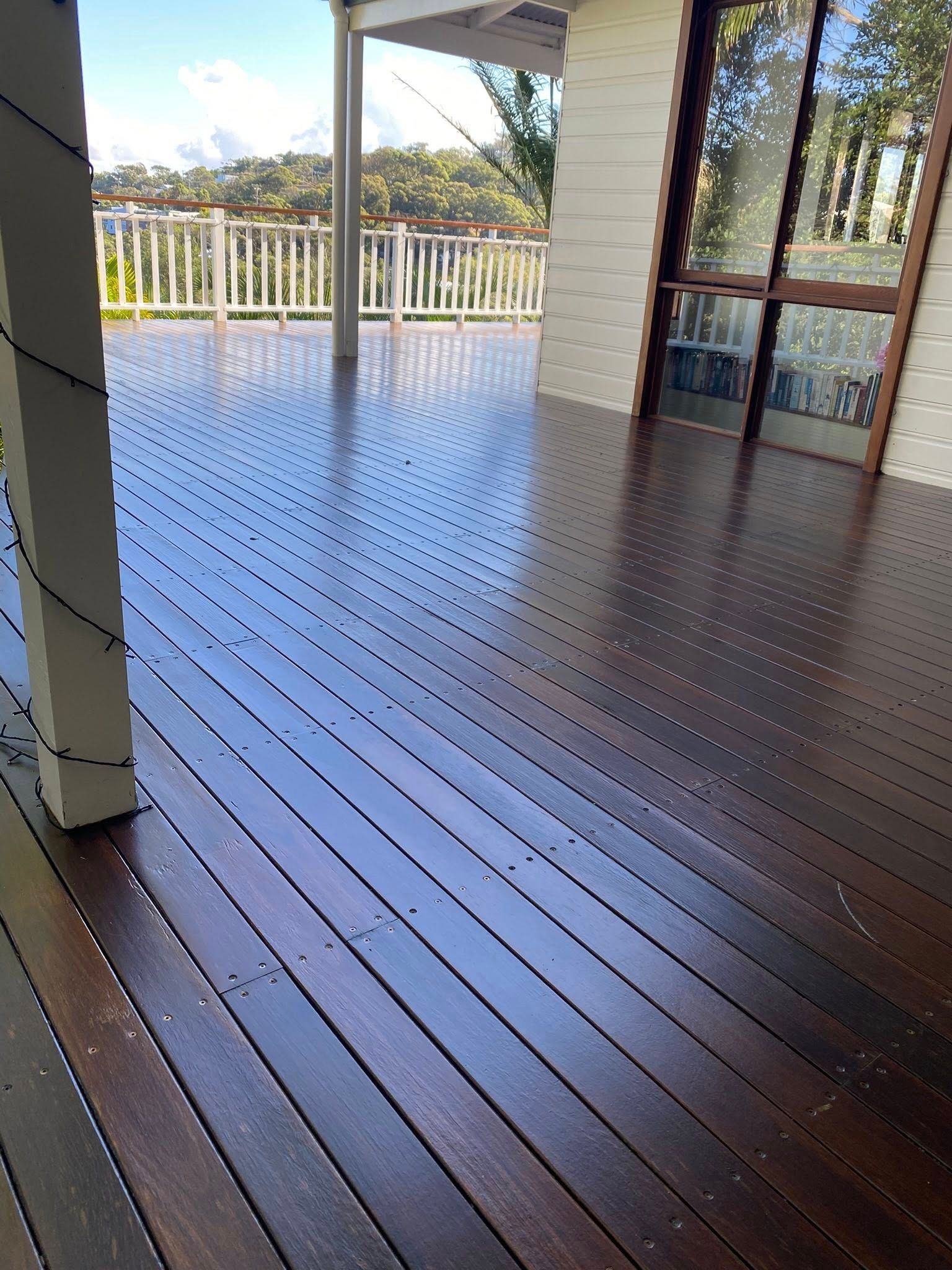 A dark-stained wooden deck with a radiating pattern of screws, viewed from a porch looking toward a white railing — Custom Floor Sanding In Somersby, NSW