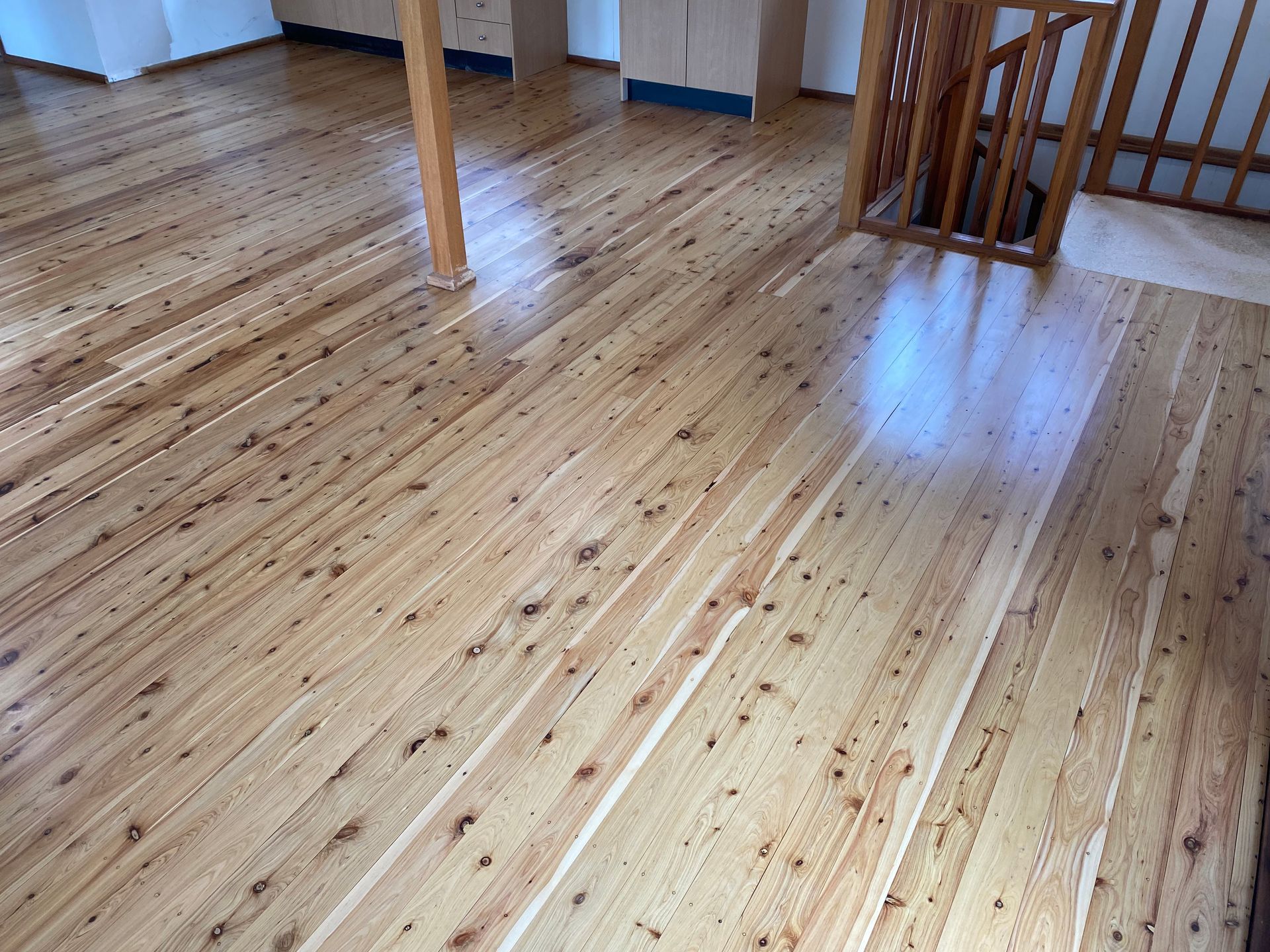 Empty polished wood floor in a bright room with a small railing and table legs — Custom Floor Sanding In Somersby, NSW
