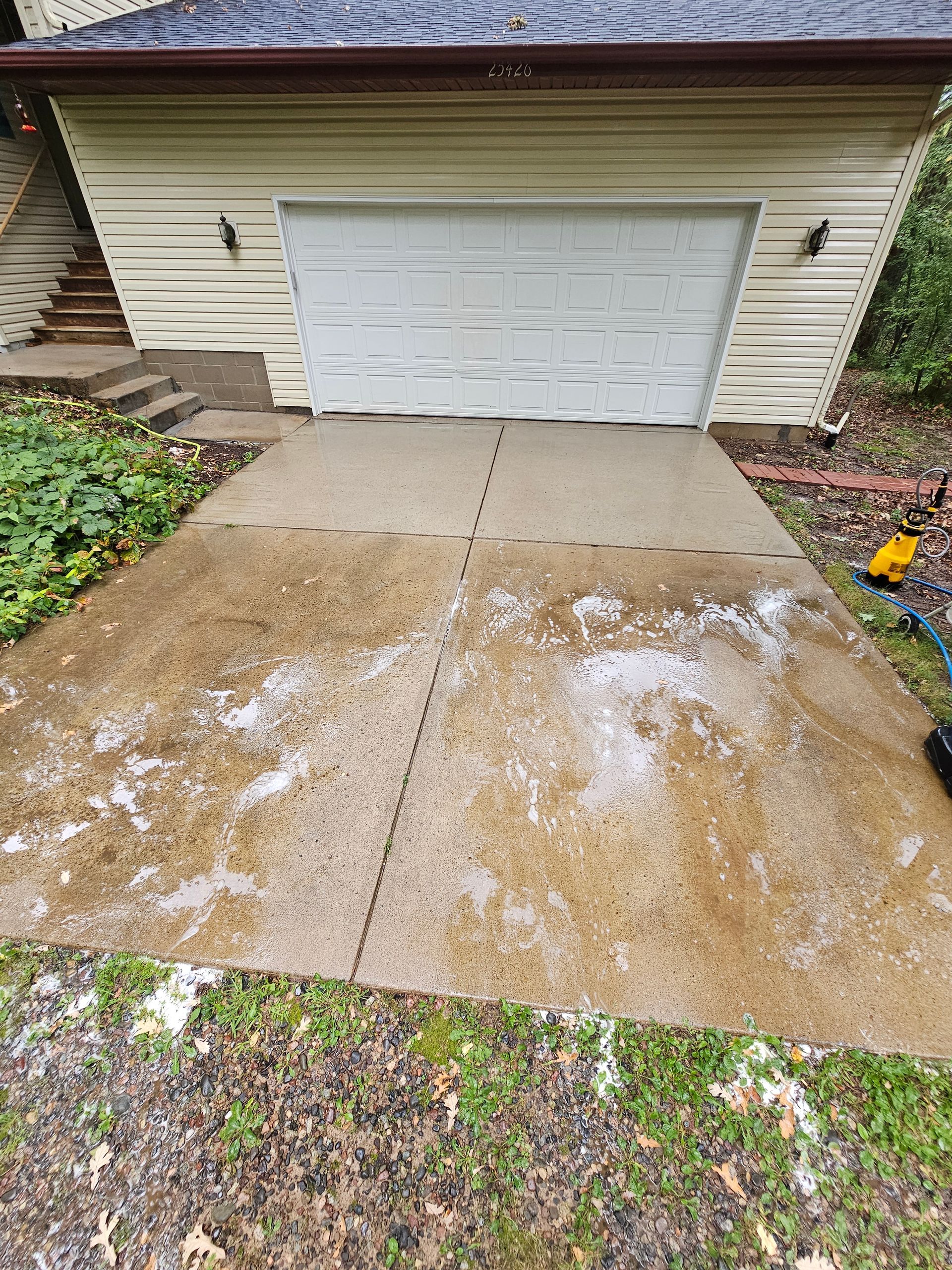 Person power washing a stone patio with a green pressure washer outdoors, sunlight.