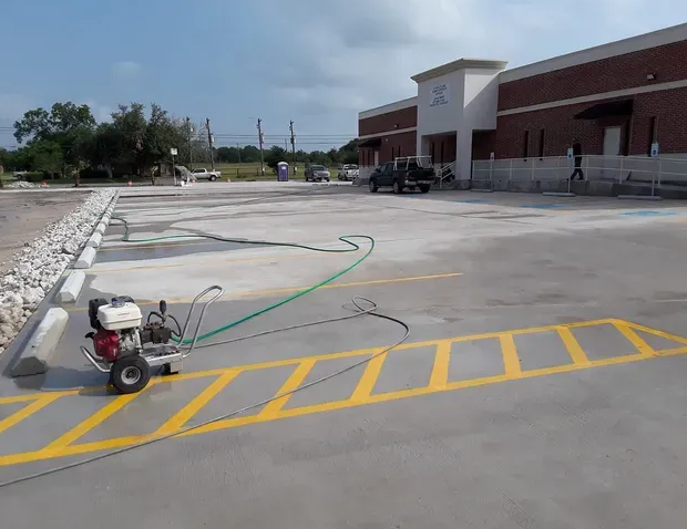 Parking lot striping in progress; yellow lines painted on concrete with a striping machine. Building in background.