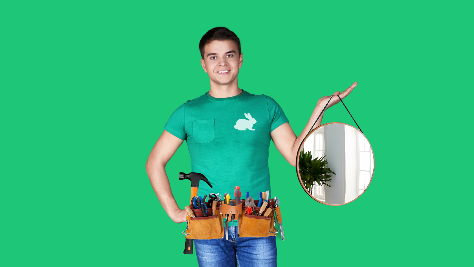 A smiling person in a green shirt and tool belt holds a round hanging mirror against a solid green background.
