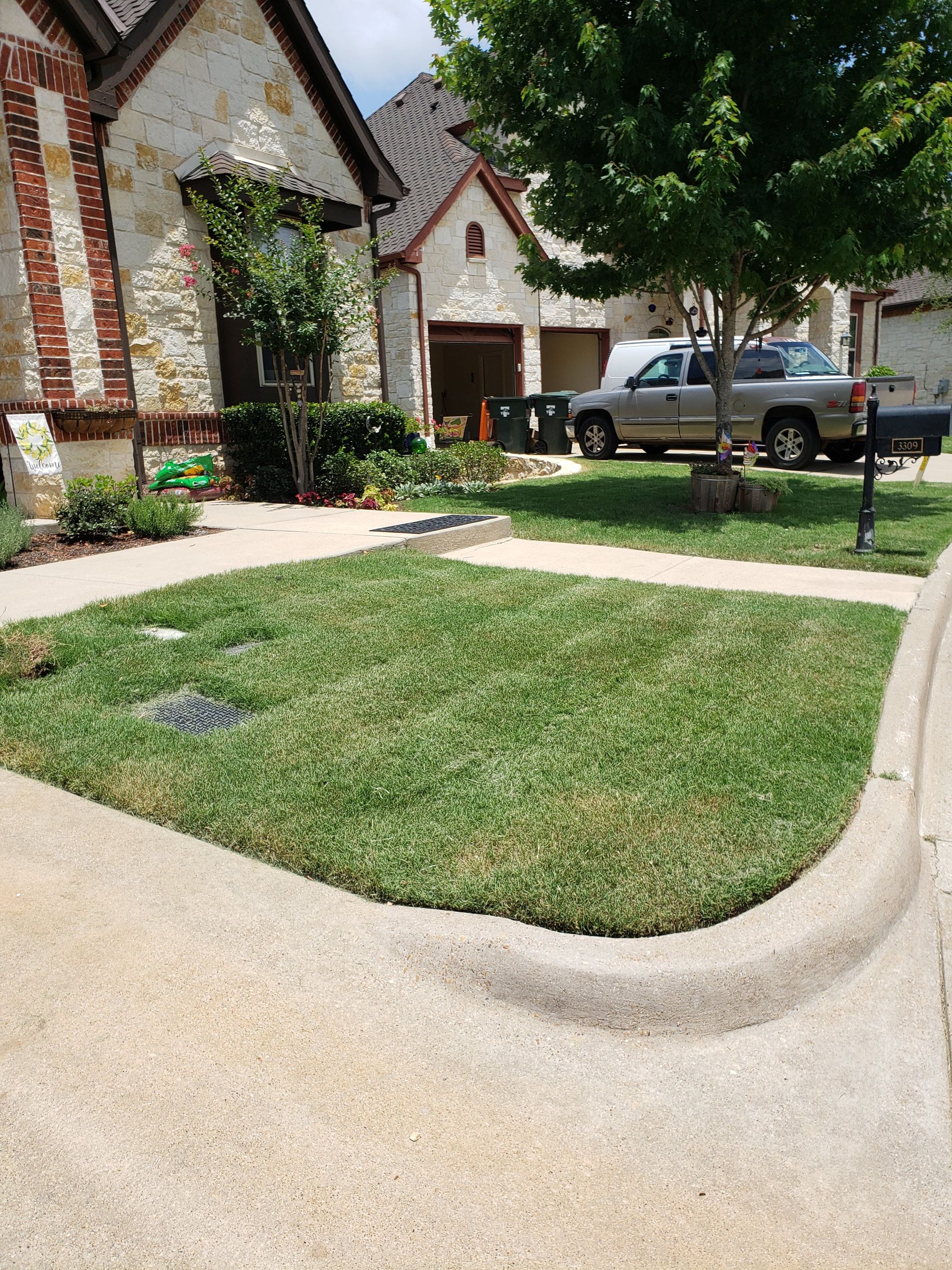 A suburban stone home with a small lawn, a paved driveway, and a parked silver SUV, viewed from a street curb.