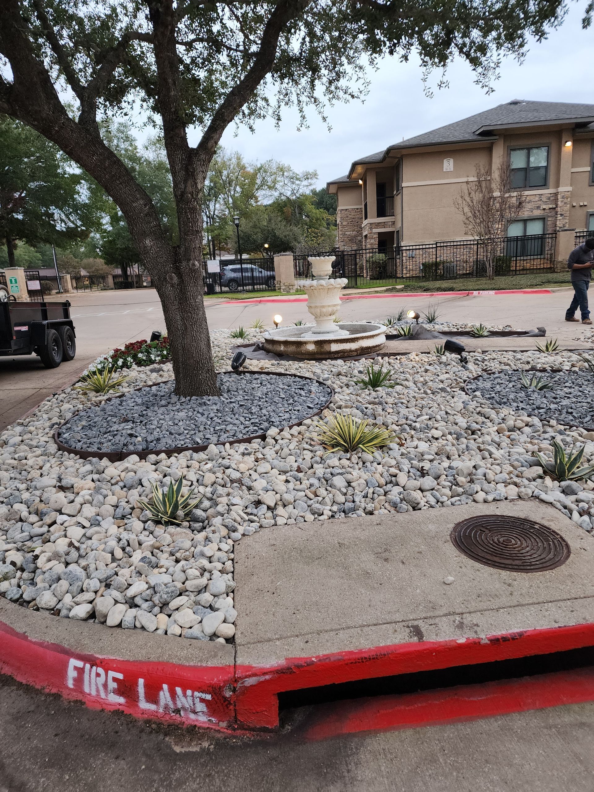A landscaped island features a stone fountain and tree surrounded by grey rocks, marked by a red 