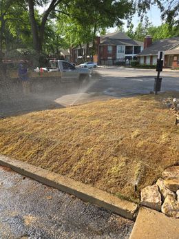 A sprinkler waters a patch of freshly mulched dirt and gravel in front of a residential apartment building.
