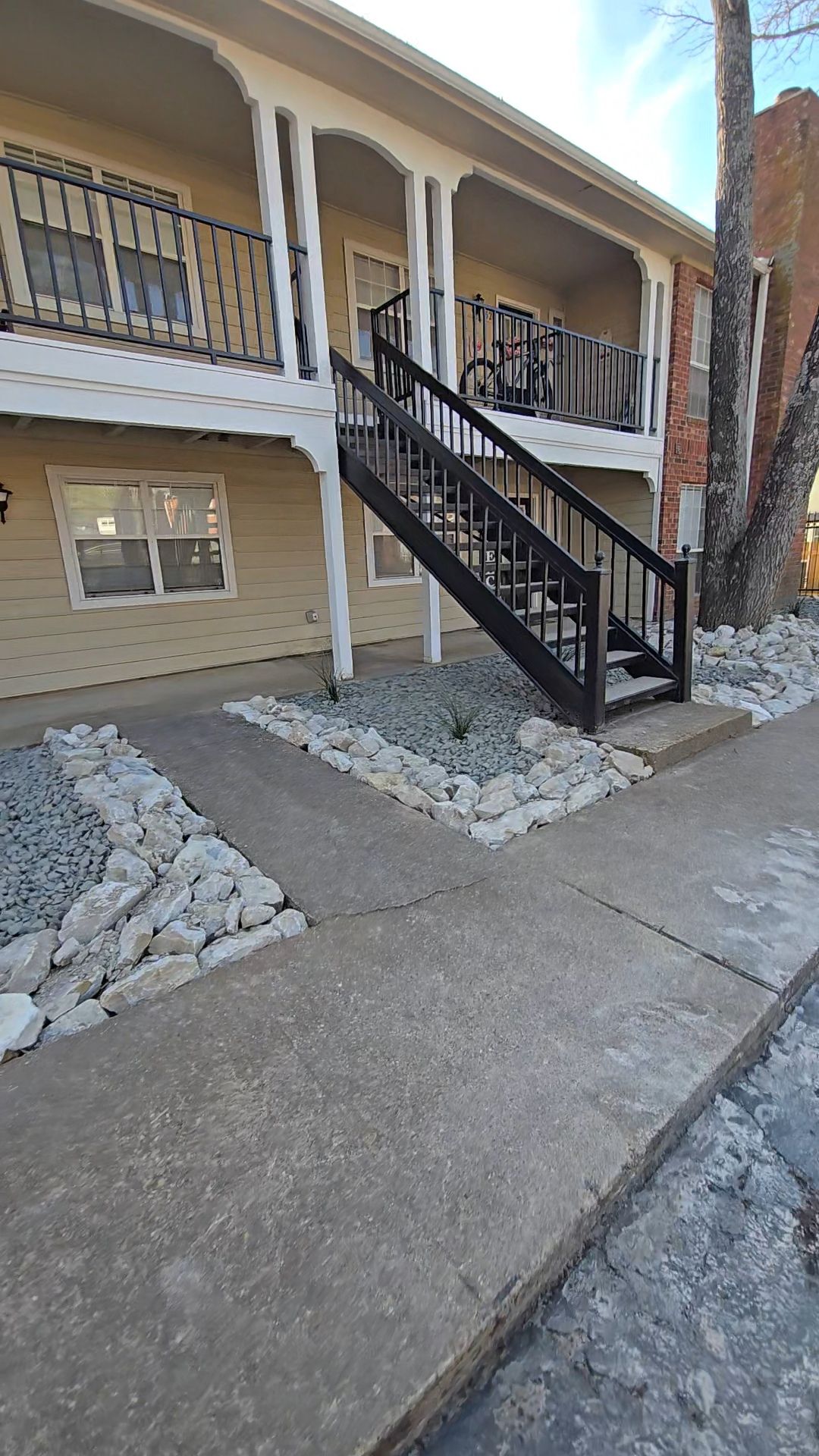 A beige two-story apartment building with a dark wooden exterior staircase leading to the second-floor balcony.