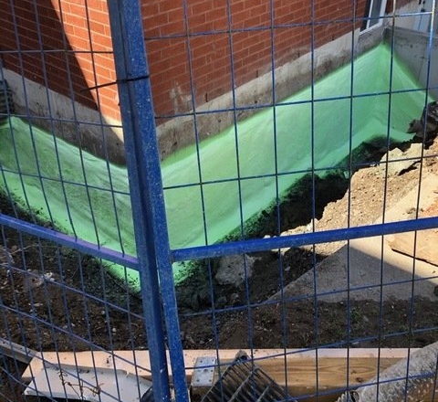 Blue fence around a green and tan fenced-off area with dark debris along the edge