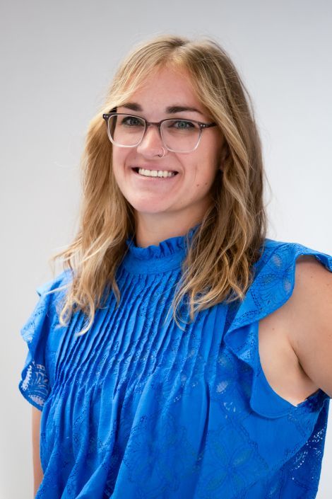 A woman wearing glasses and a blue top is smiling for the camera.