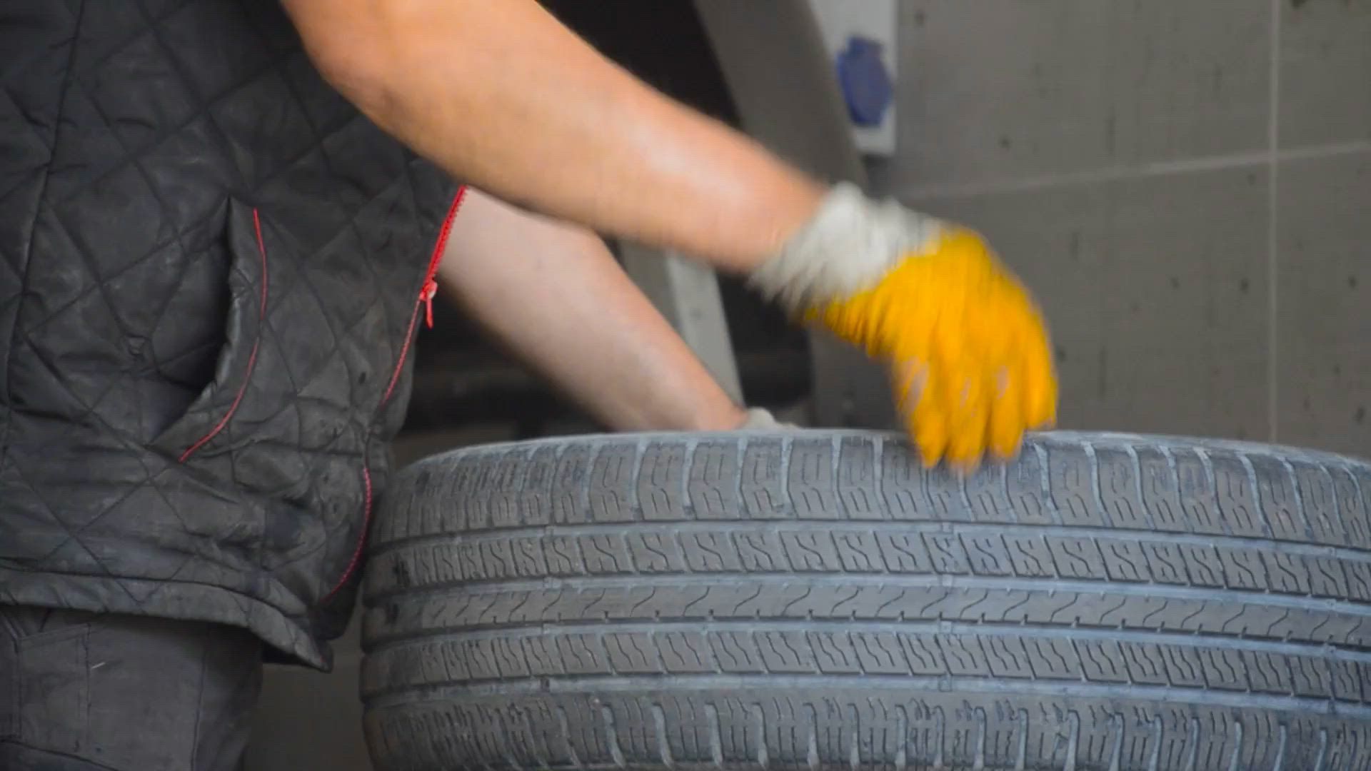 Una persona con un gilet grigio e un guanto arancione impila pneumatici in un garage