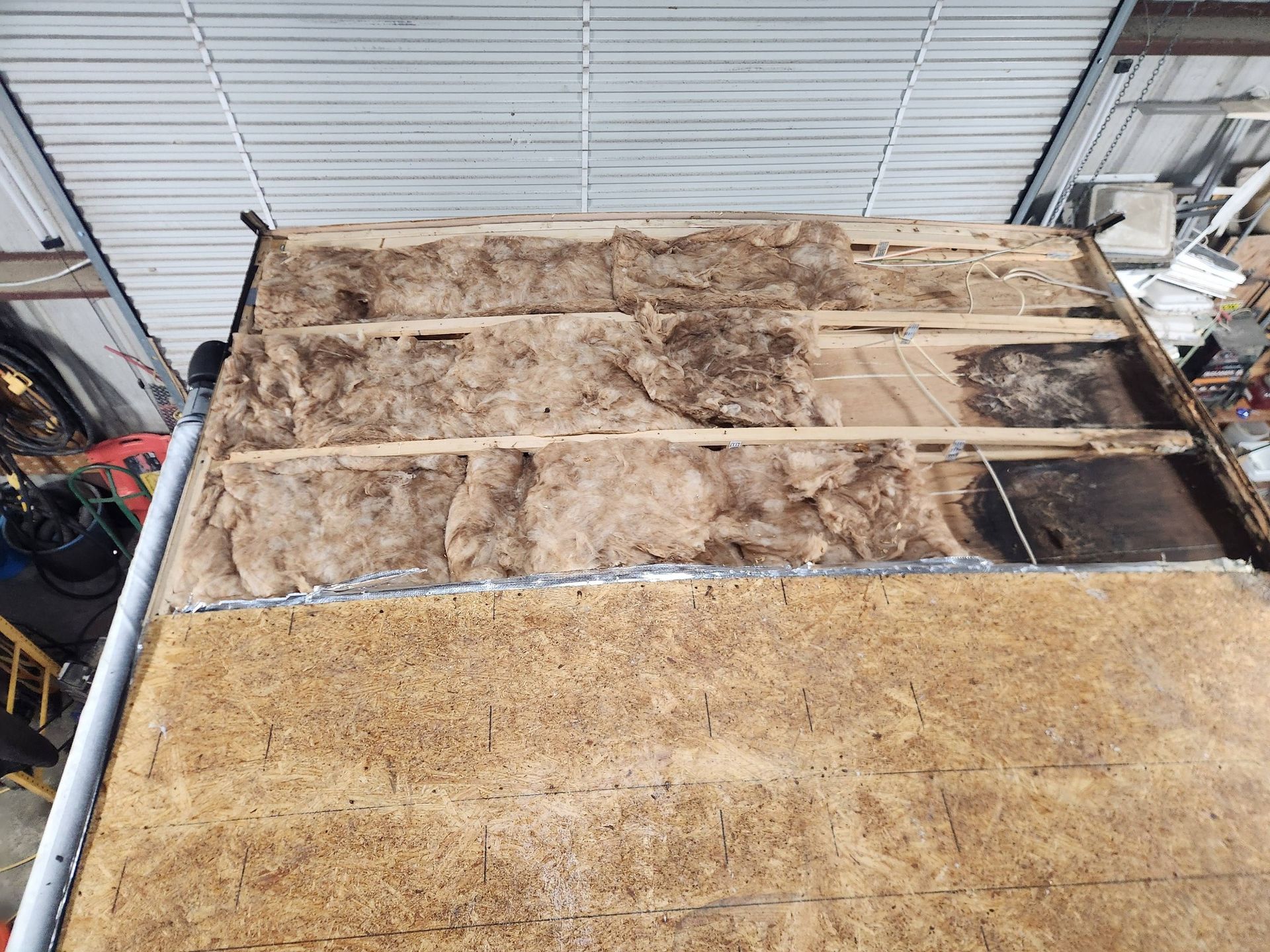 Partially stripped roof with exposed insulation and damaged sections beside a metal-sided building