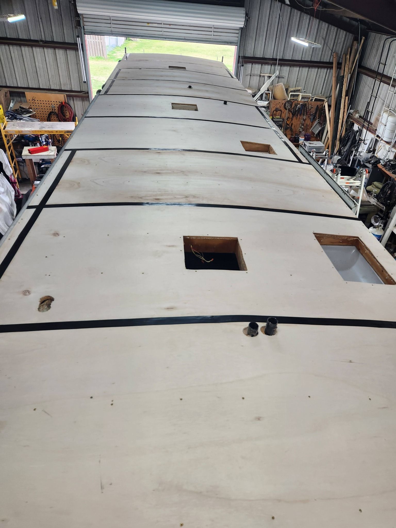 Long white industrial panel or wing section inside a workshop, viewed from above with square cutouts and equipment nearby