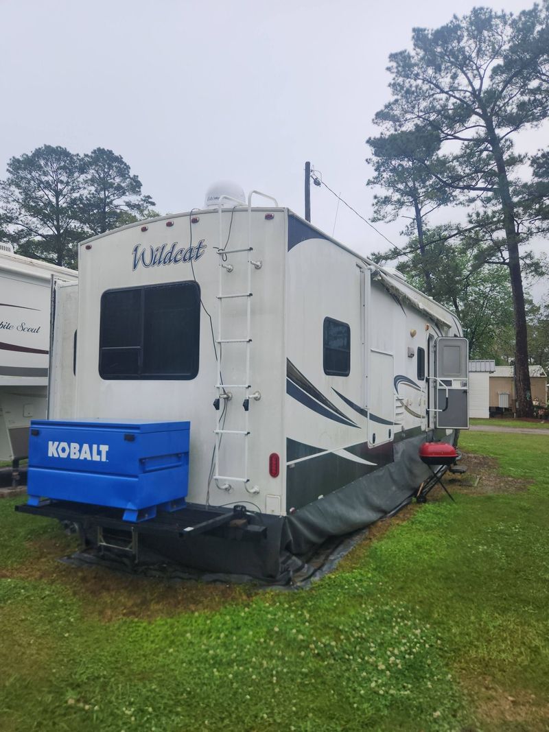 White Keystone travel trailer with blue cargo box parked on grass under cloudy sky
